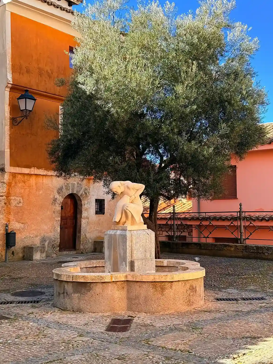 Plaza de Cuenca con fuente de piedra, escultura blanca y olivo entre fachadas ocres. Foto propia La Maleta Inquieta
