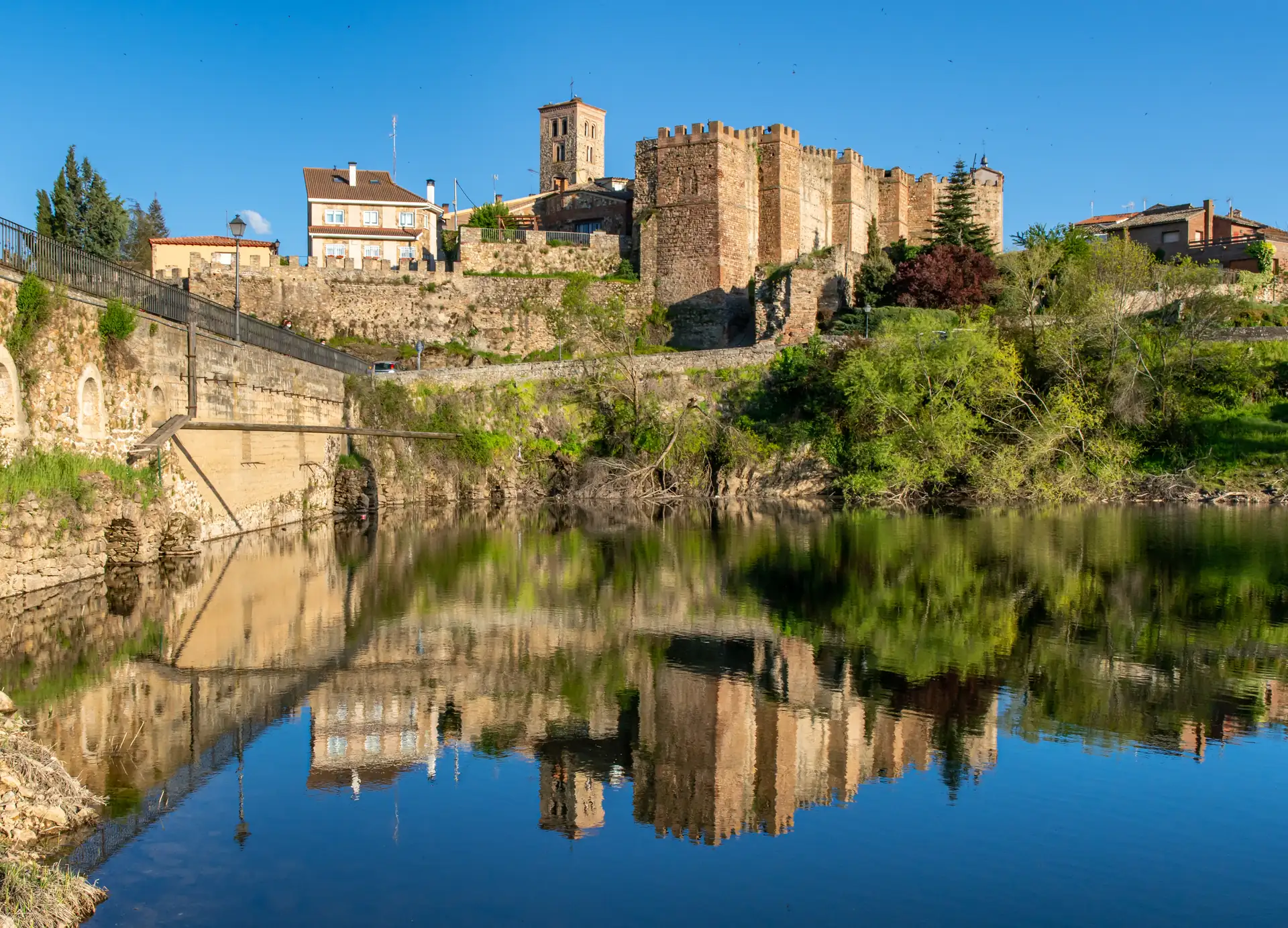 Muralla y castillo de Buitrago del Lozoya reflejados en el río en un día soleado, La Maleta Inquieta