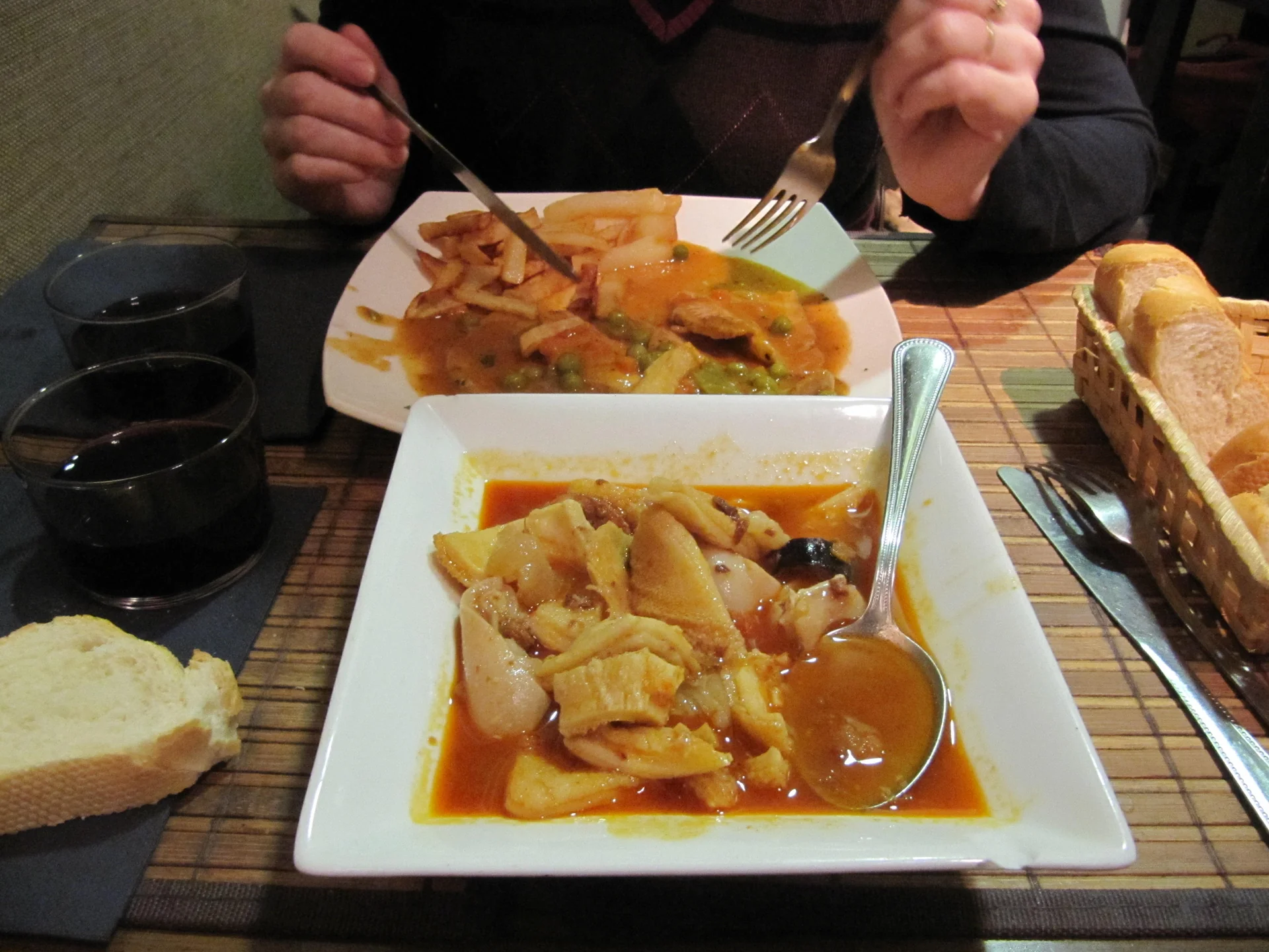Plato de callos a la madrileña en salsa roja junto a una cesta de pan, en la mesa de un restaurante