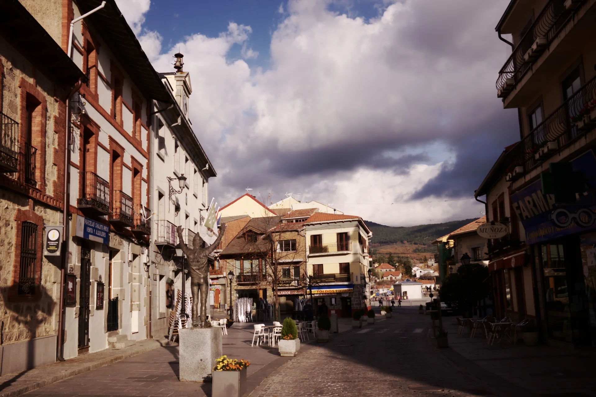 Calle empedrada de Cercedilla con edificios tradicionales y la sierra al fondo bajo nubes