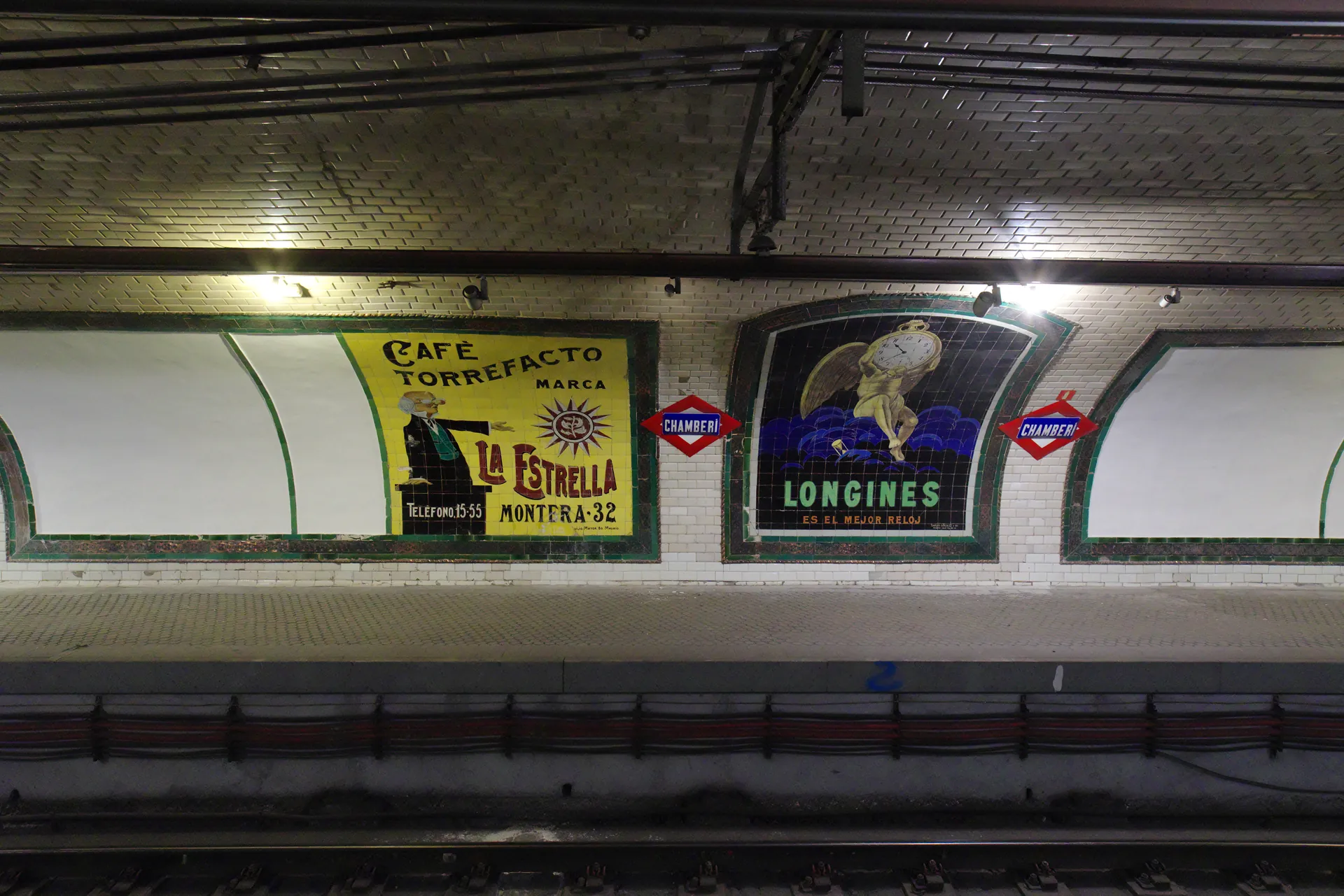 Andén de la estación de Chamberí con anuncios de azulejos de Café La Estrella y Longines junto a las vías