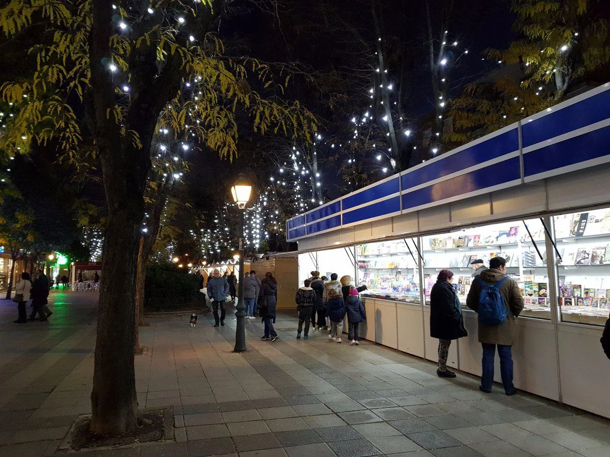 Casetas de un mercadillo de Navidad con adornos y luces en una plaza porticada de Madrid