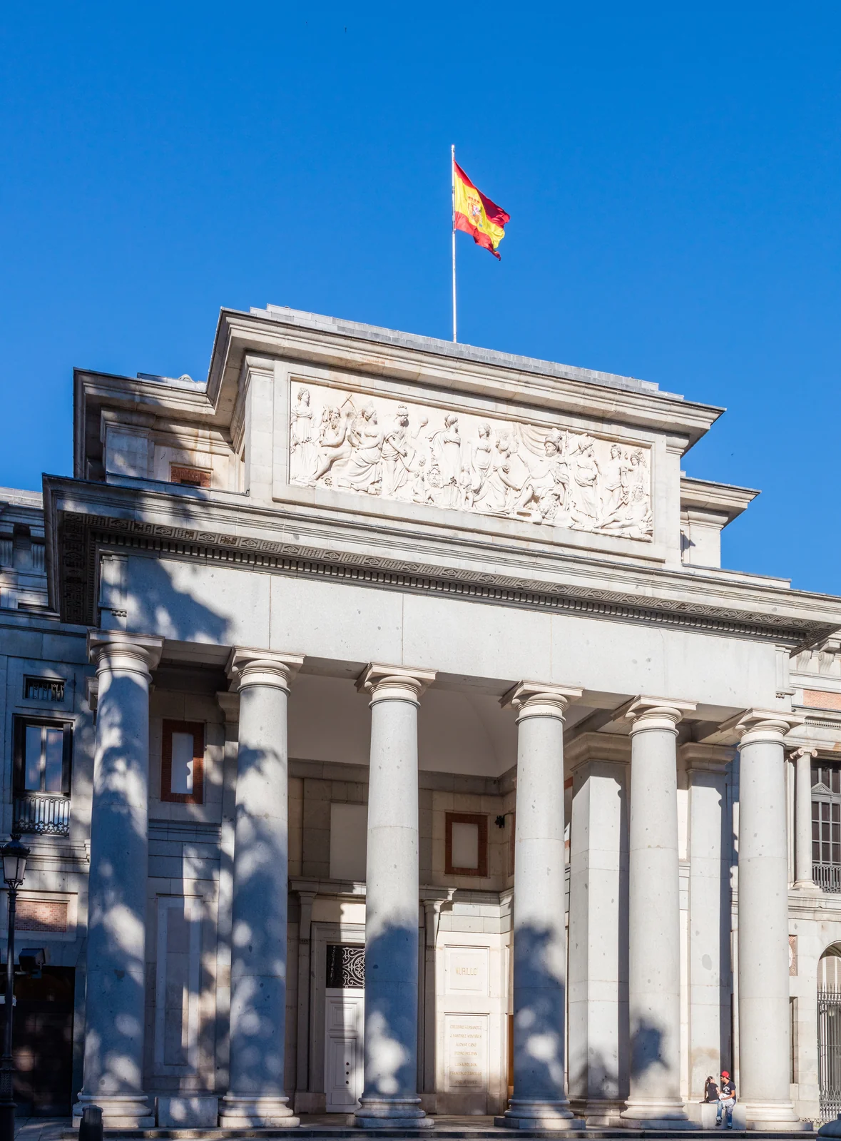 Fachada neoclasica de piedra del Museo del Prado en Madrid, con su portico de columnas doricas y la bandera de Espana
