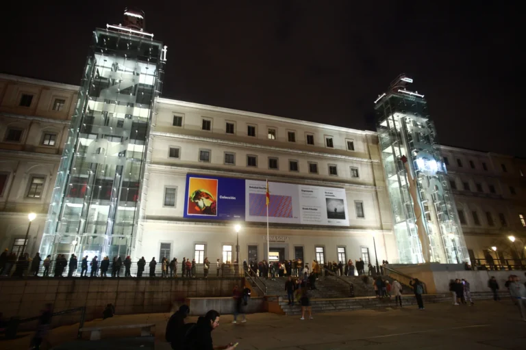 Museo Reina Sofía de noche con sus torres de ascensores de cristal iluminadas y cola de visitantes — La Maleta Inquieta