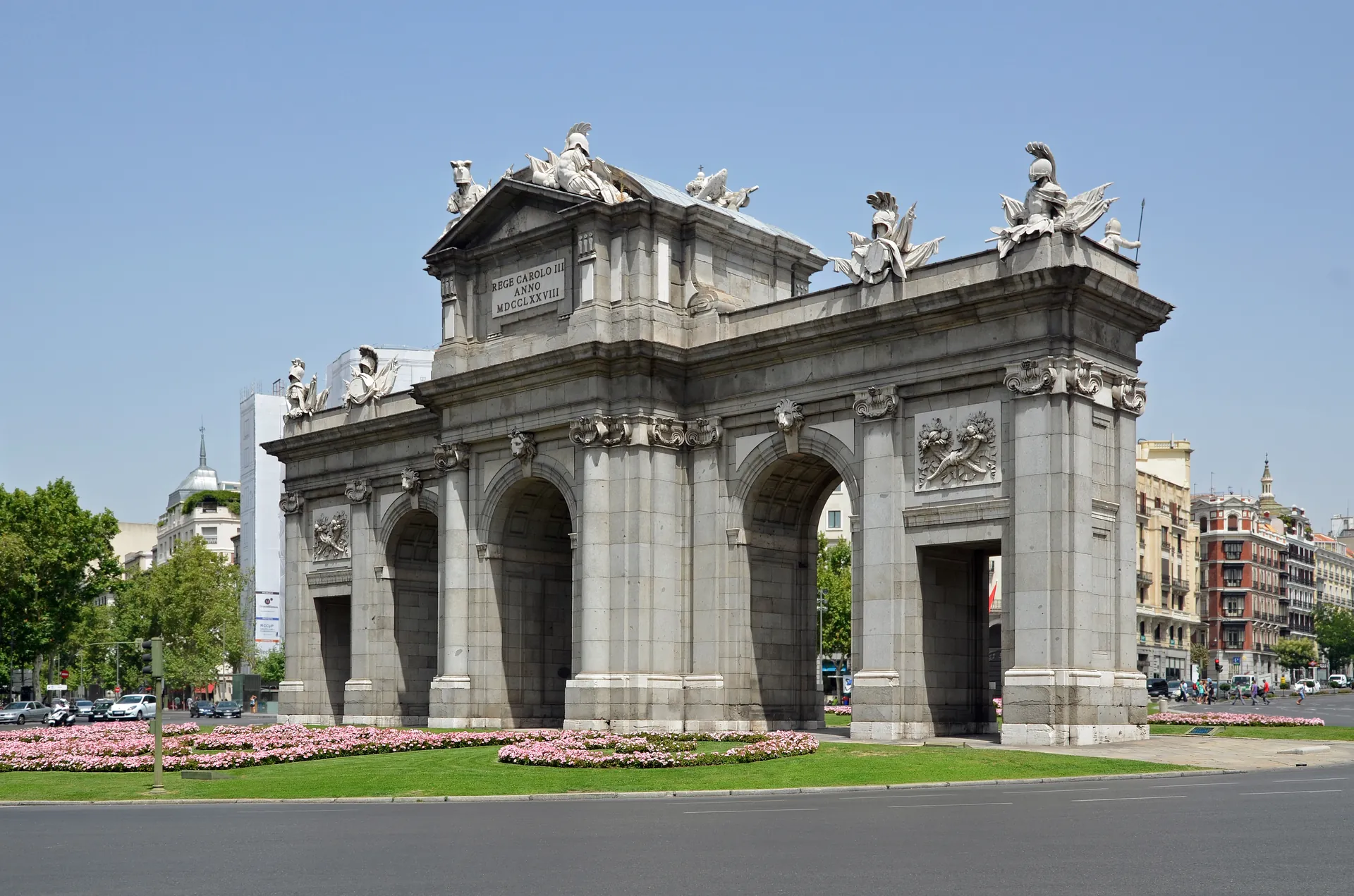 Puerta de Alcalá de Madrid, arco de granito con esculturas rodeado de jardines con flores en la plaza de la Independencia