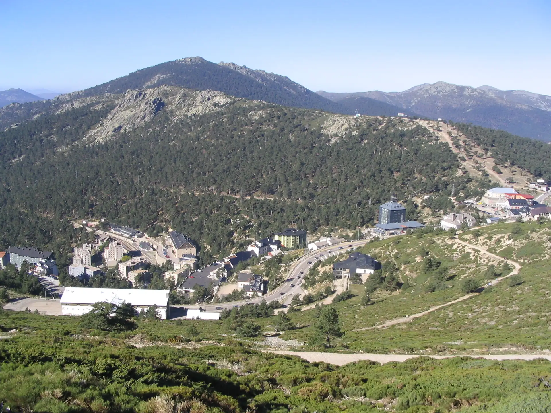 Vista aérea del Puerto de Navacerrada con edificios entre pinos y montañas de la sierra
