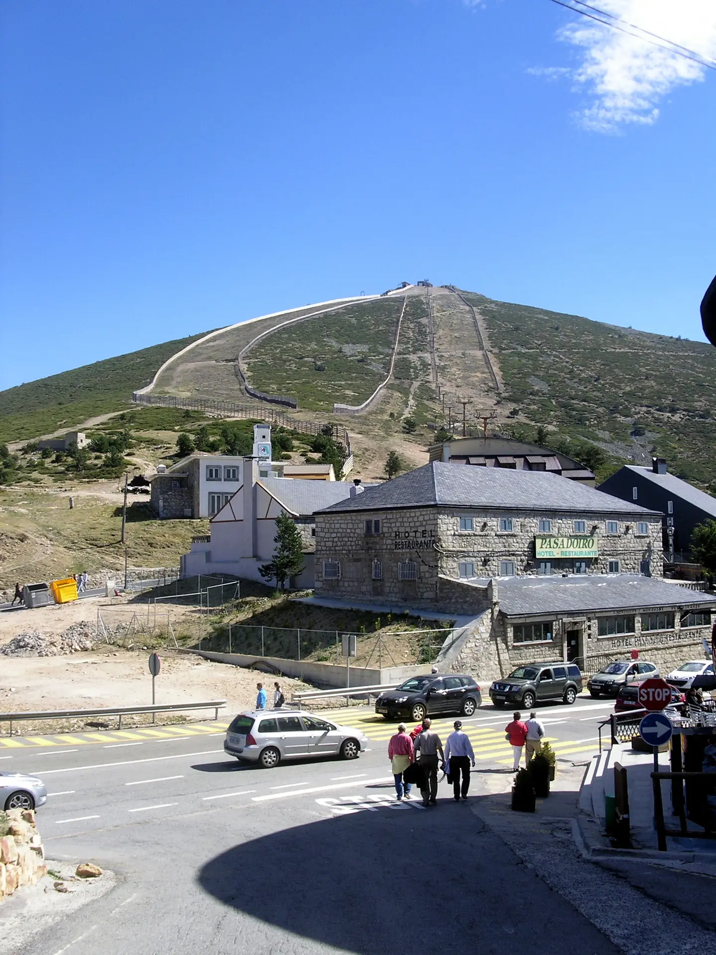 Hotel-restaurante de piedra junto a la carretera del Puerto de Navacerrada, con la ladera de una pista sin nieve y los postes de un telesilla detrás.