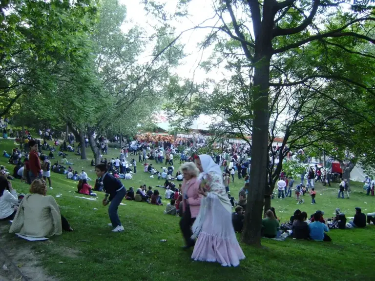 Gente en la pradera de San Isidro de Madrid con mujer vestida de chulapa y árboles