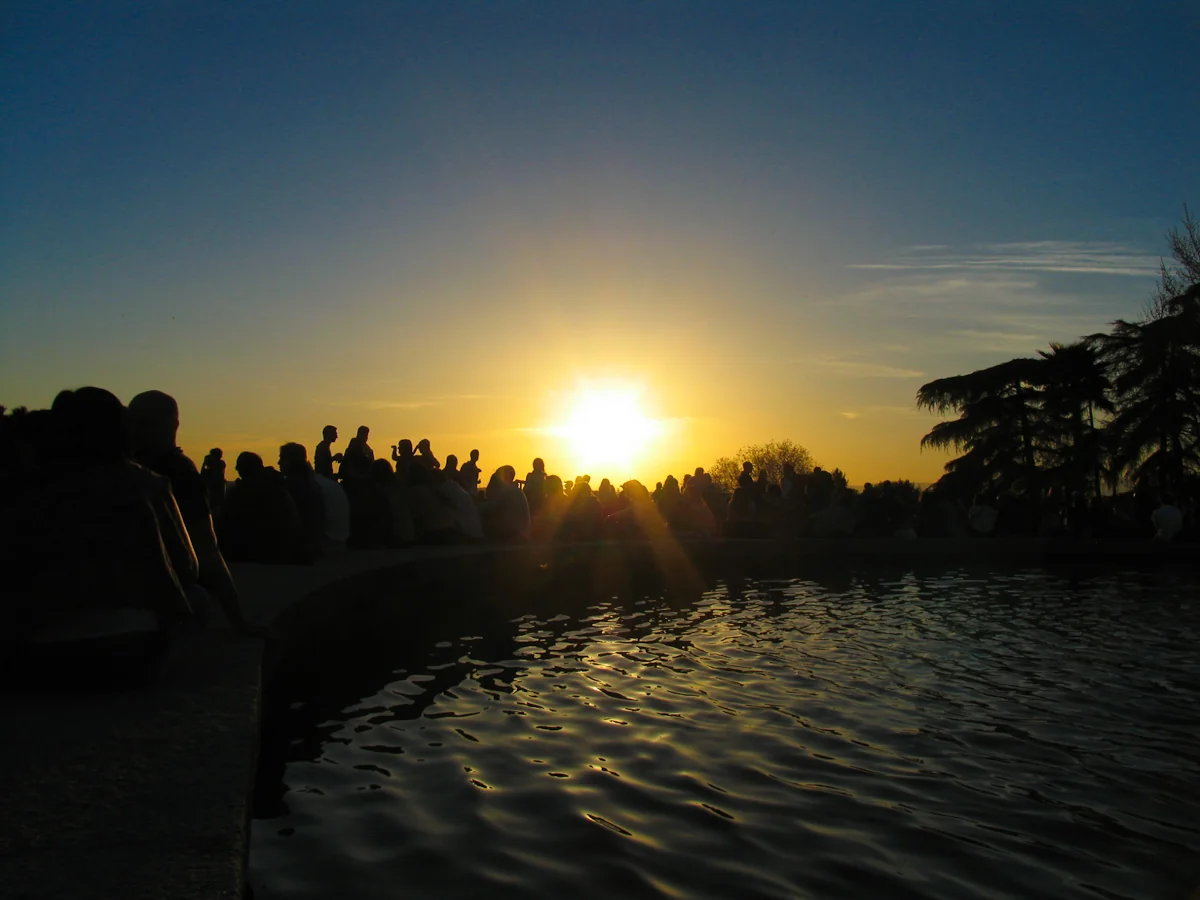 Siluetas de gente junto al estanque del Templo de Debod mientras el sol se pone detrás, con el agua brillando