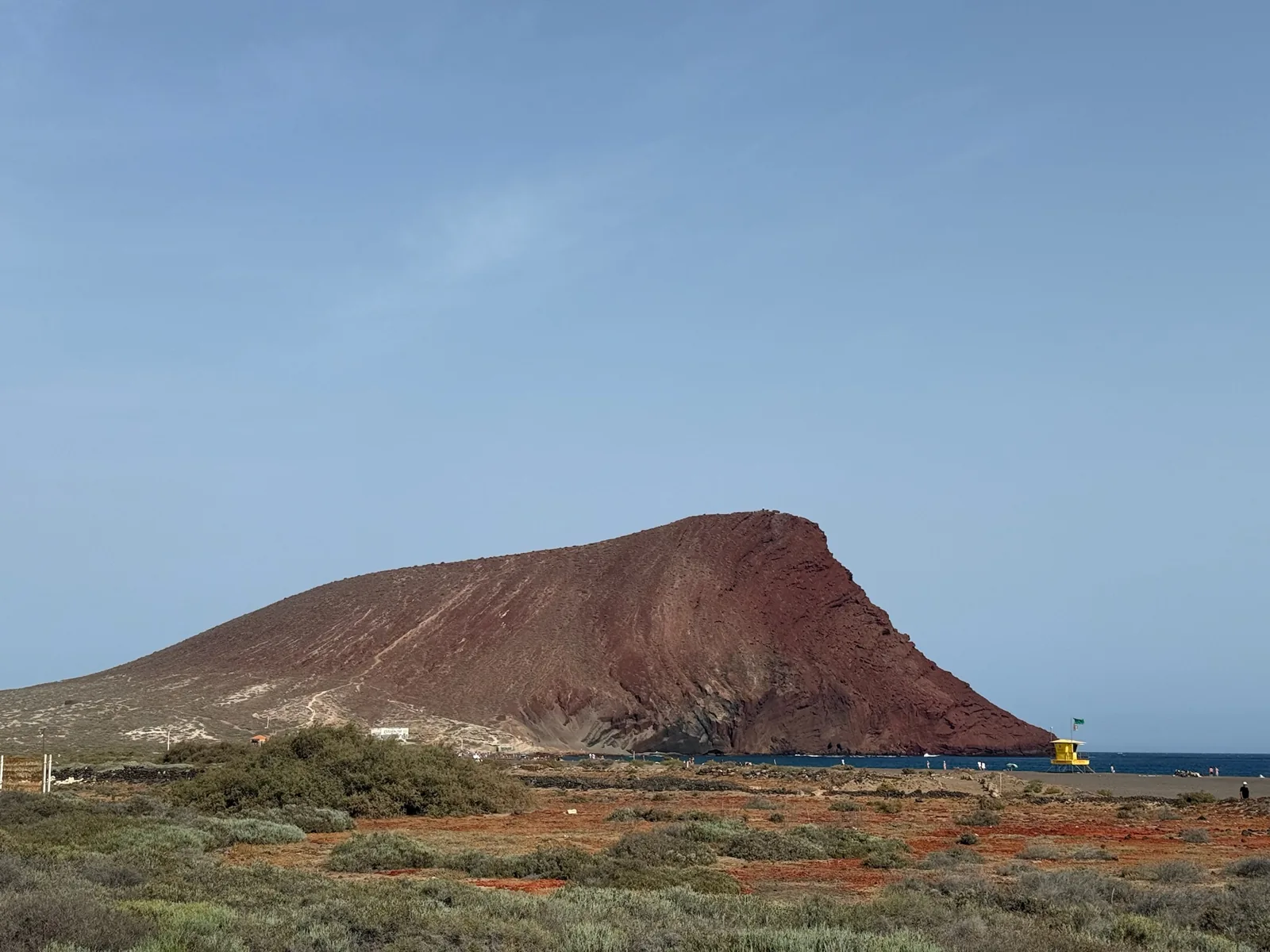 El cono rojizo de Montaña Roja sobre la playa de La Tejita al atardecer, con la arena y el mar en penumbra. Foto propia La Maleta Inquieta, agosto 2026.