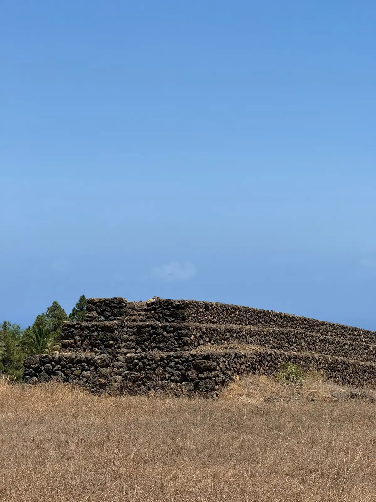 Pirámide escalonada de piedra volcánica en Güímar con hierba seca alrededor. Foto propia La Maleta Inquieta, agosto 2026.