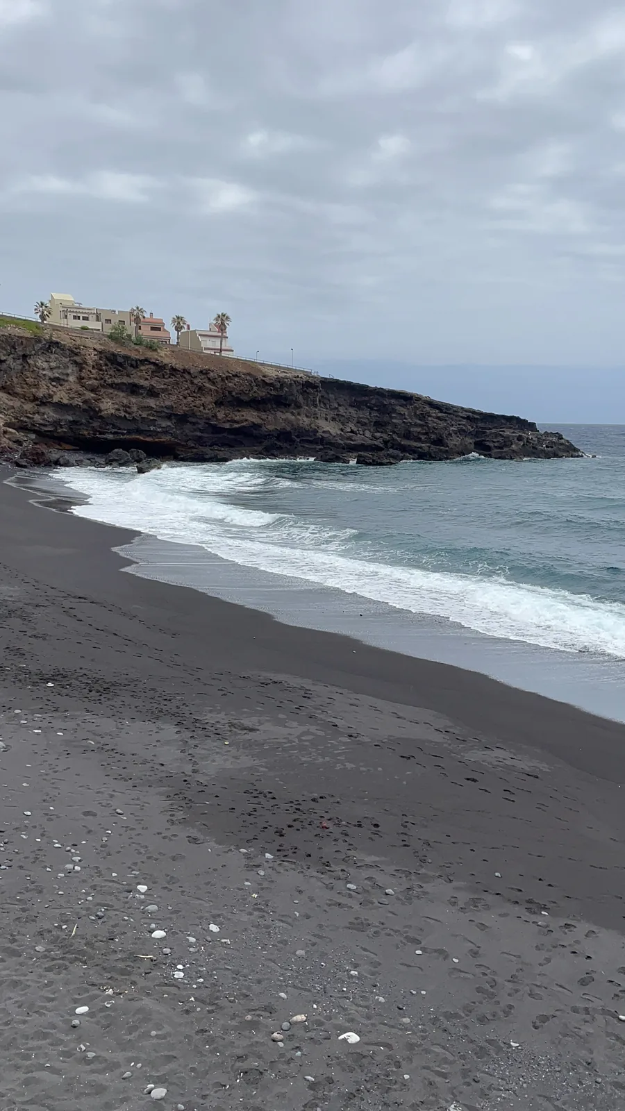 Playa de arena volcánica negra con olas y edificios costeros en el Puertito de Güímar. Foto propia La Maleta Inquieta, agosto 2026.