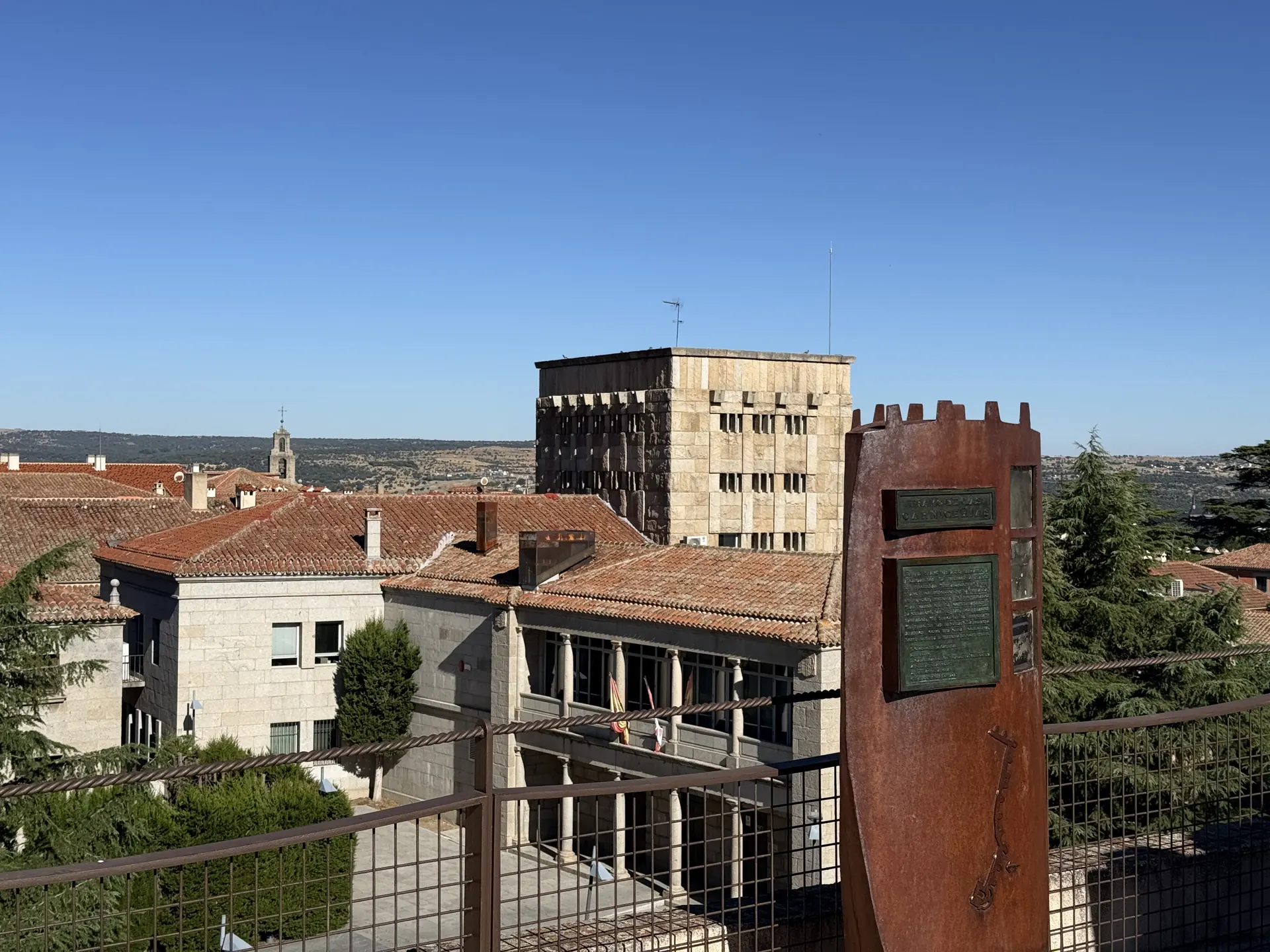 Panel almenado de acero oxidado del tramo de las Carnicerías en el adarve de Ávila, con tejados y la sierra detrás. Foto propia La Maleta Inquieta, septiembre 2026.