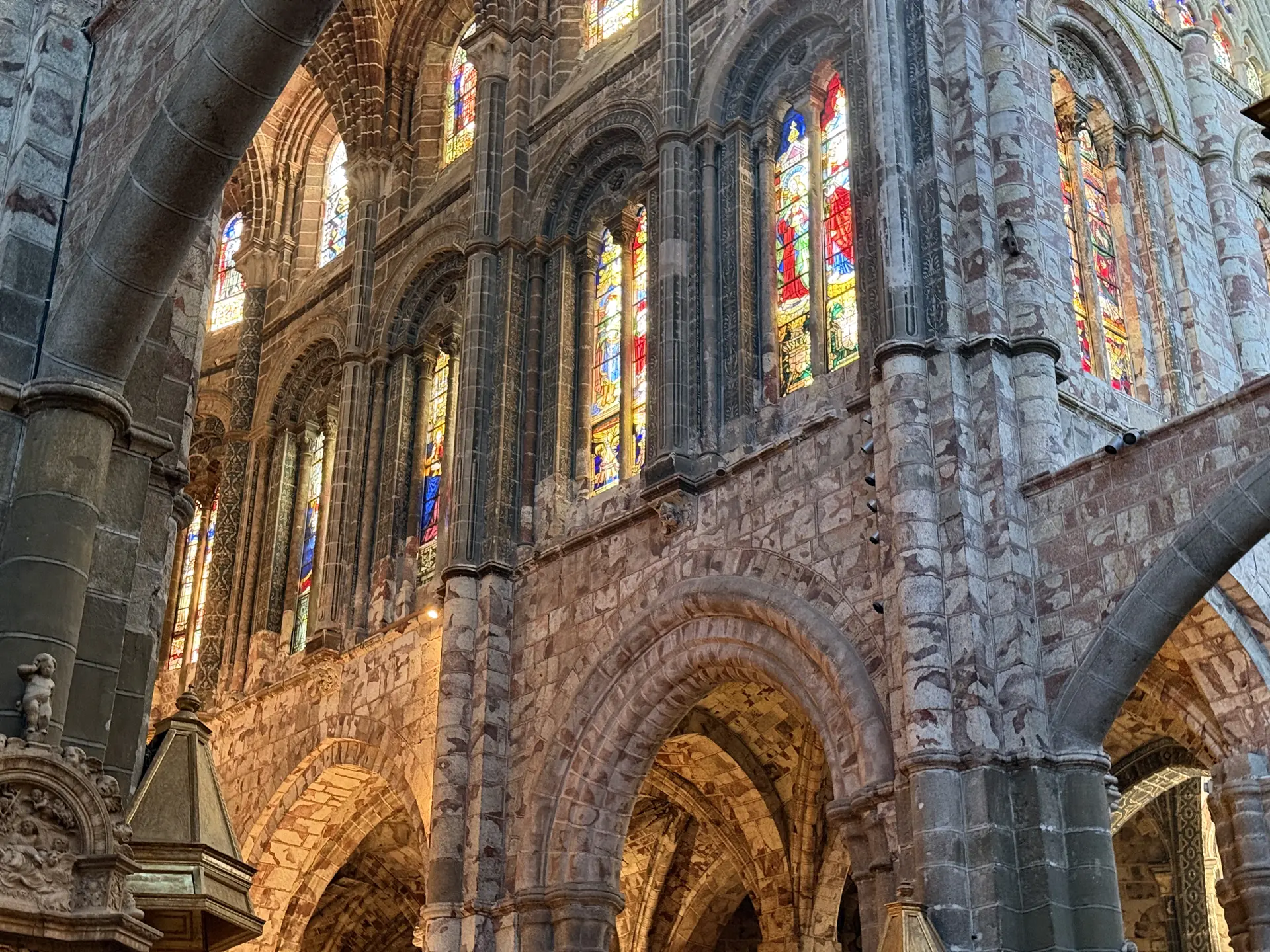 Vidrieras de colores sobre los arcos de la girola en piedra sangrante roja y blanca, en la catedral de Ávila. Foto propia La Maleta Inquieta, septiembre 2026.