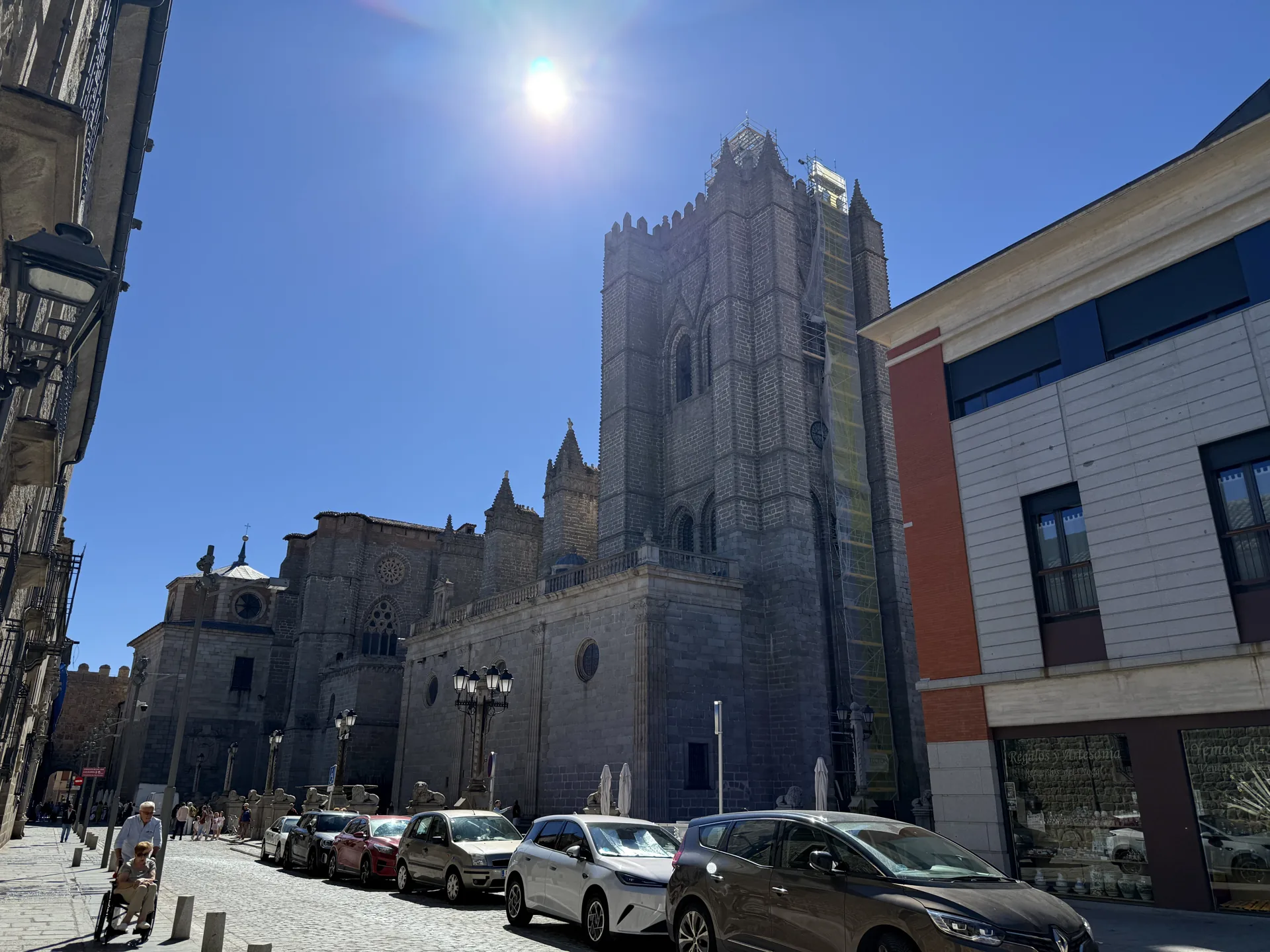 Catedral de Ávila a contraluz desde la calle de acceso a su plaza, con la torre en andamios y coches aparcados. Foto propia La Maleta Inquieta, septiembre 2026.