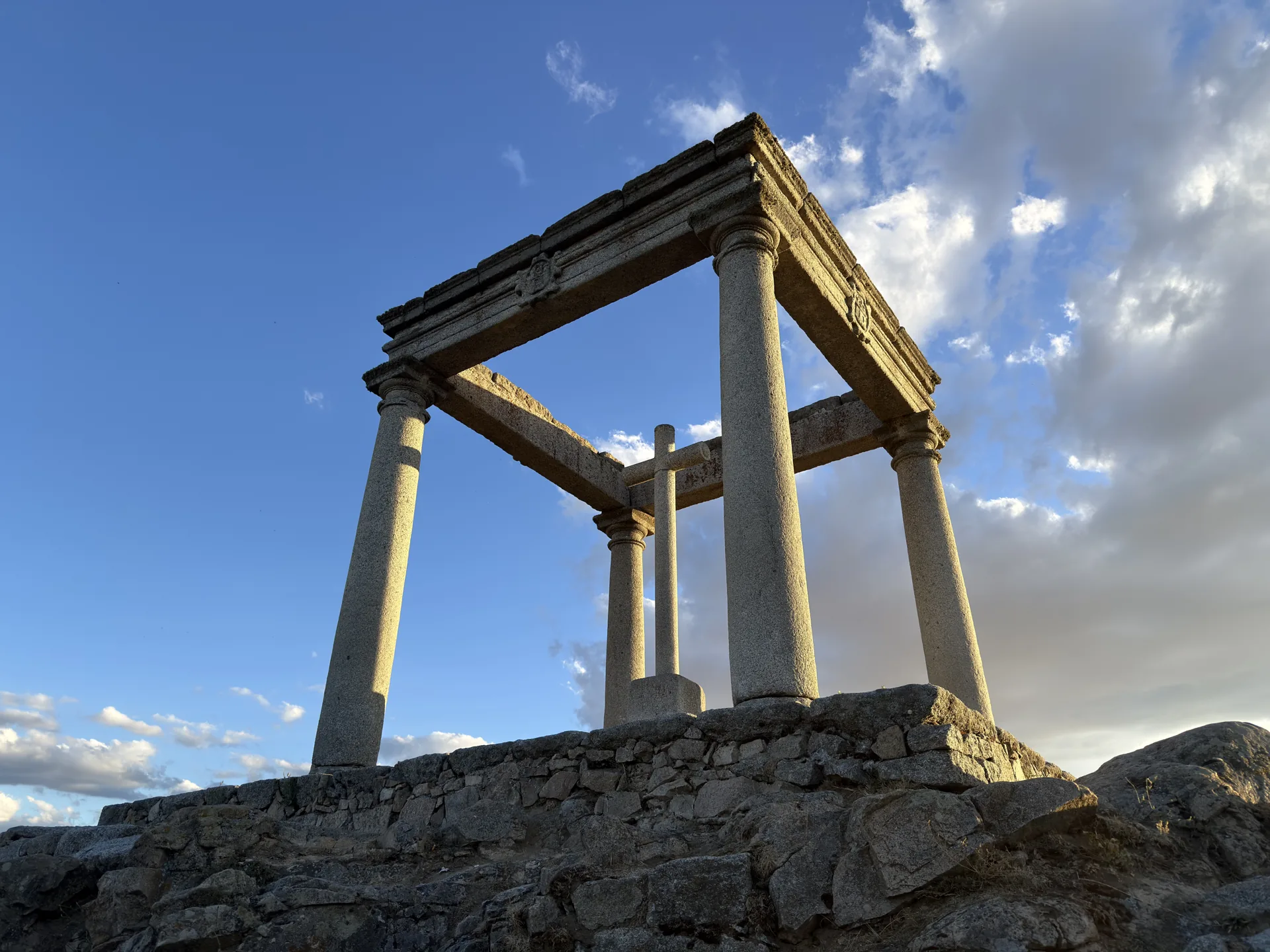 Columnas, entablamento con escudos y cruz central de Los Cuatro Postes de Ávila en contrapicado bajo las nubes. Foto propia La Maleta Inquieta, septiembre 2026.