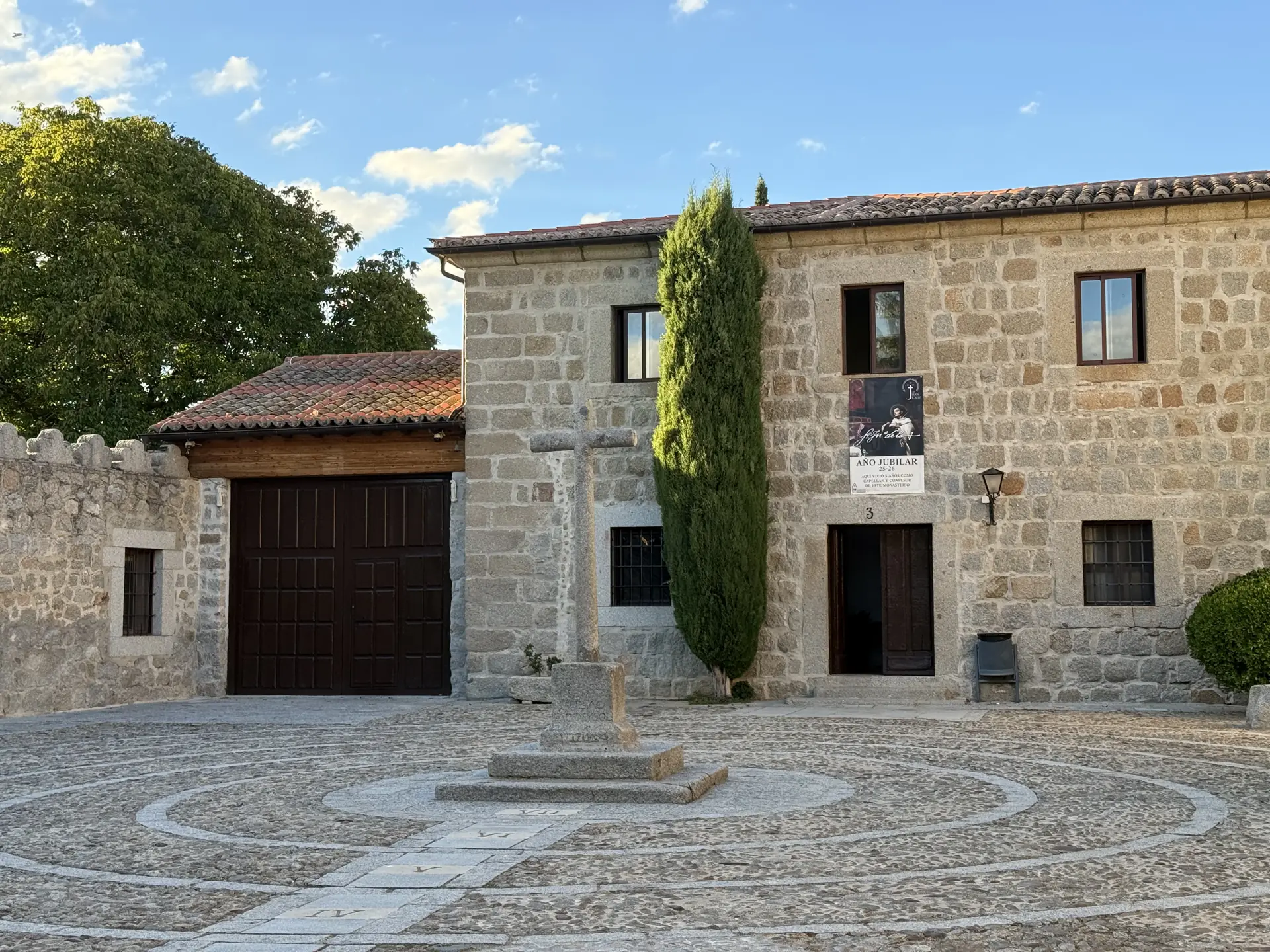 Cruz de granito sobre un empedrado circular en el compás del monasterio de la Encarnación de Ávila, con cipreses. Foto propia La Maleta Inquieta, septiembre 2026.