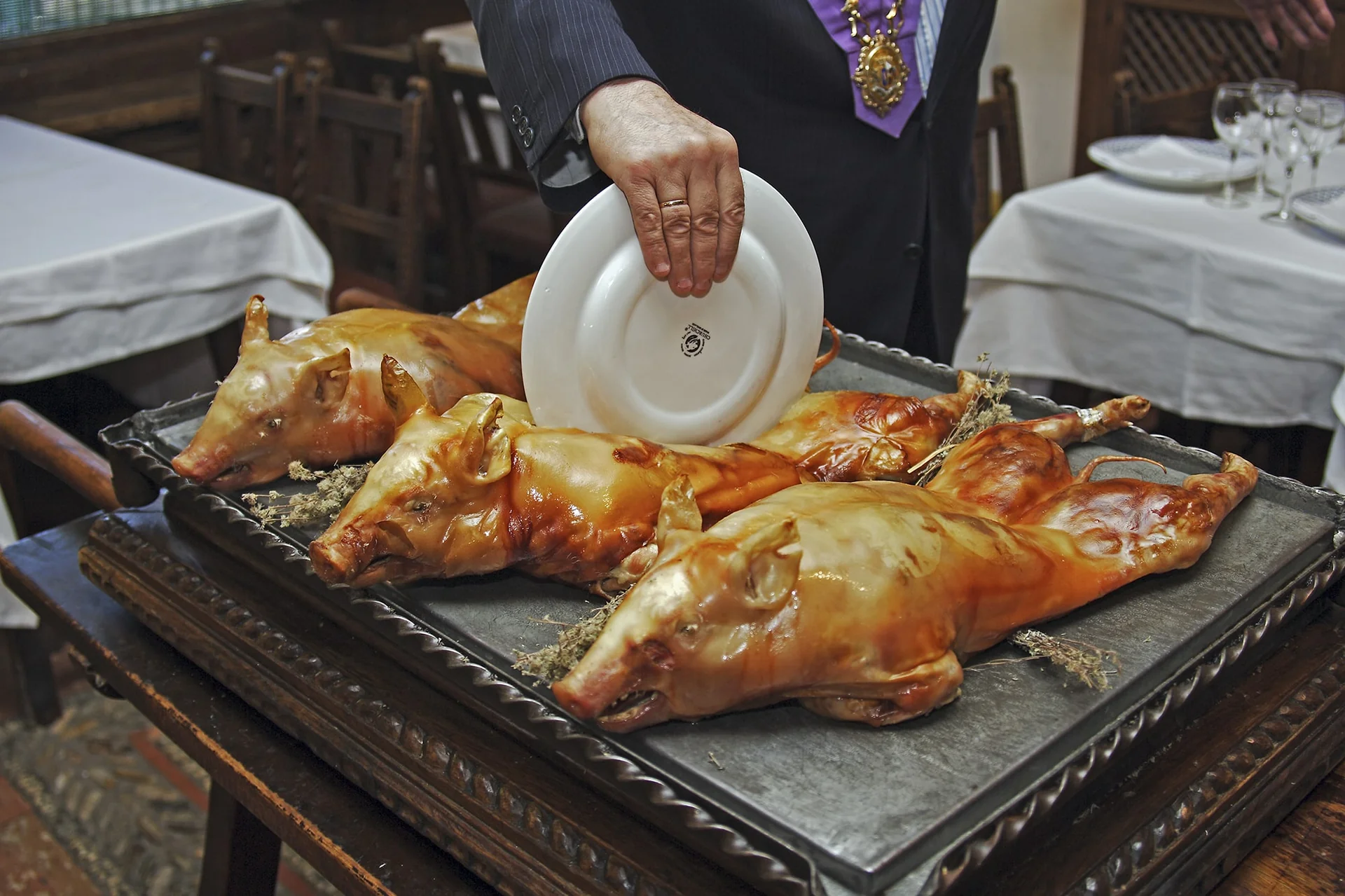 Cochinillo asado segoviano partido con el borde de un plato, con la piel dorada y crujiente
