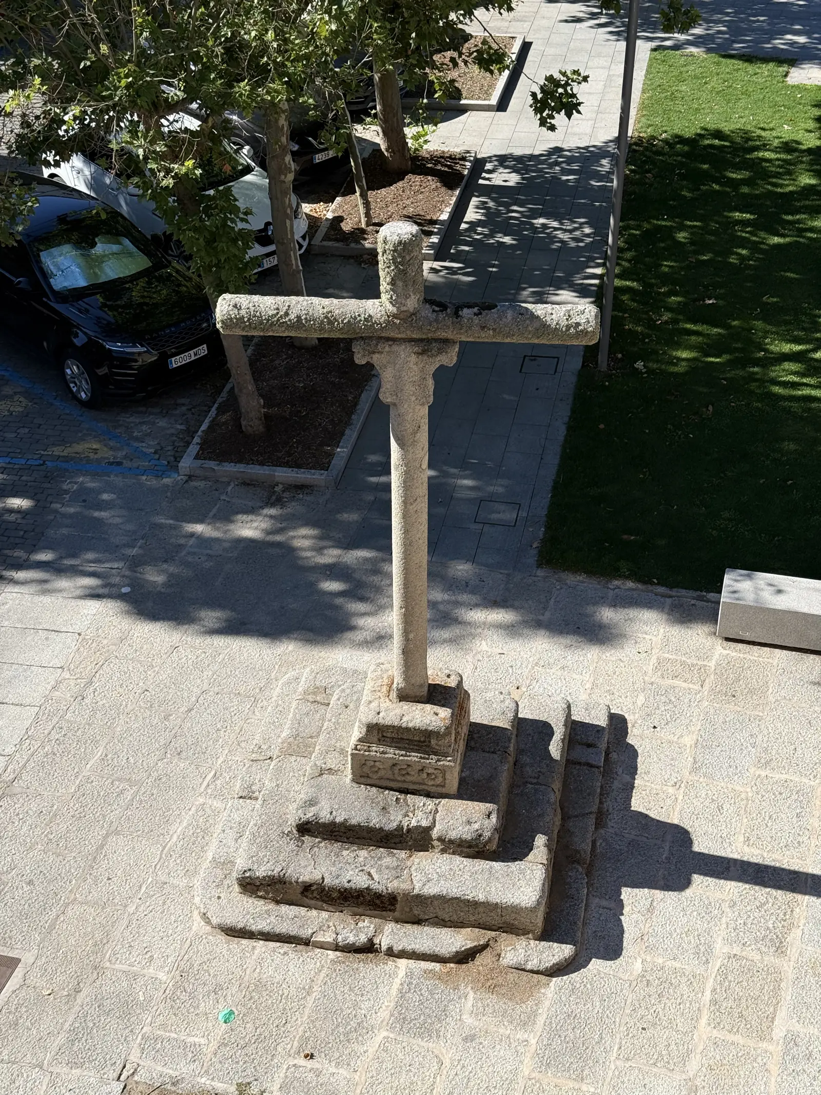 Cruz de granito sobre gradas al pie de la muralla norte de Ávila, vista en picado desde el adarve a pleno sol. Foto propia La Maleta Inquieta, septiembre 2026.
