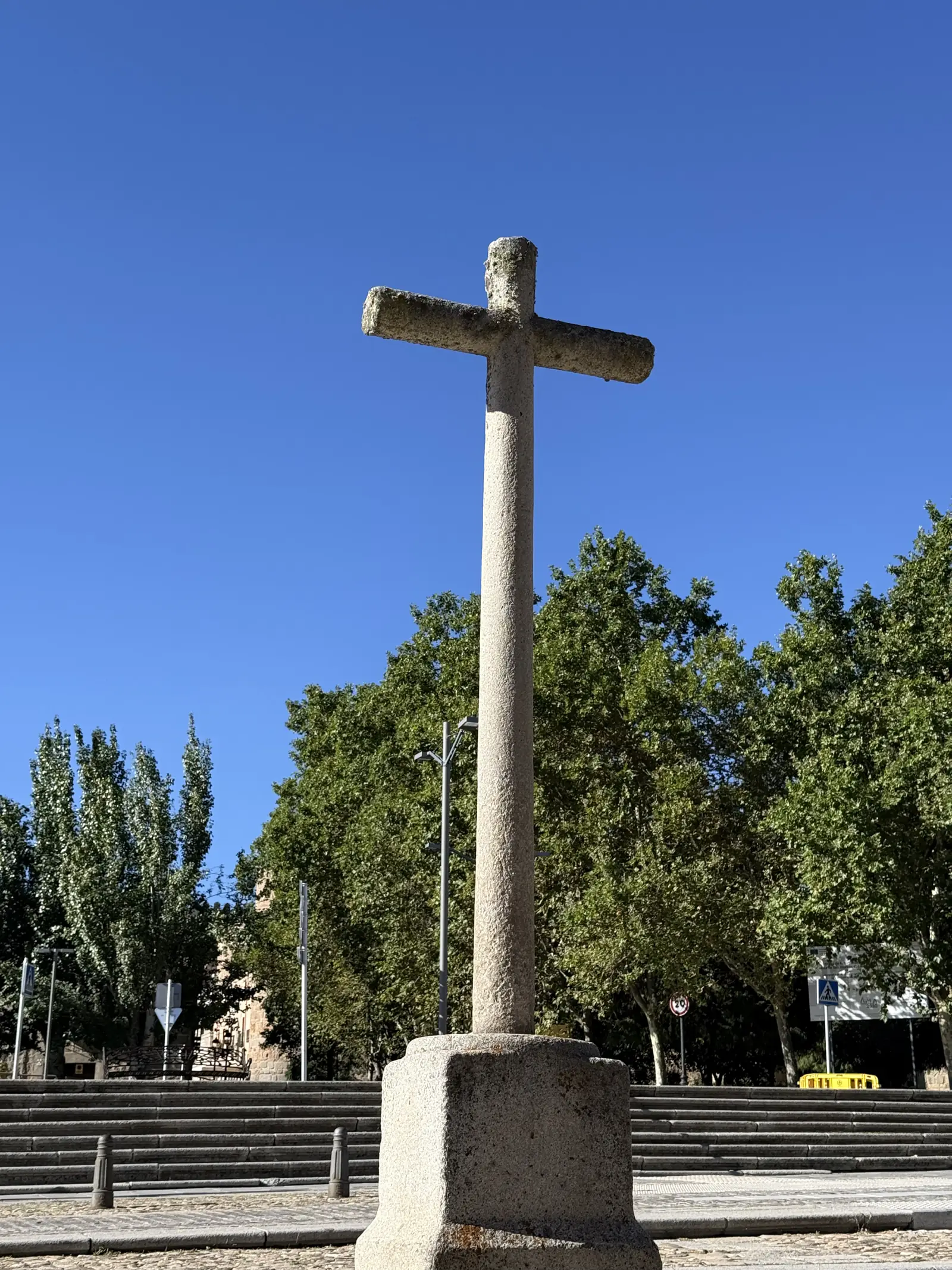 Cruz de granito sobre un pedestal cúbico en la explanada de San Vicente de Ávila, con plátanos y cielo despejado. Foto propia La Maleta Inquieta, septiembre 2026.
