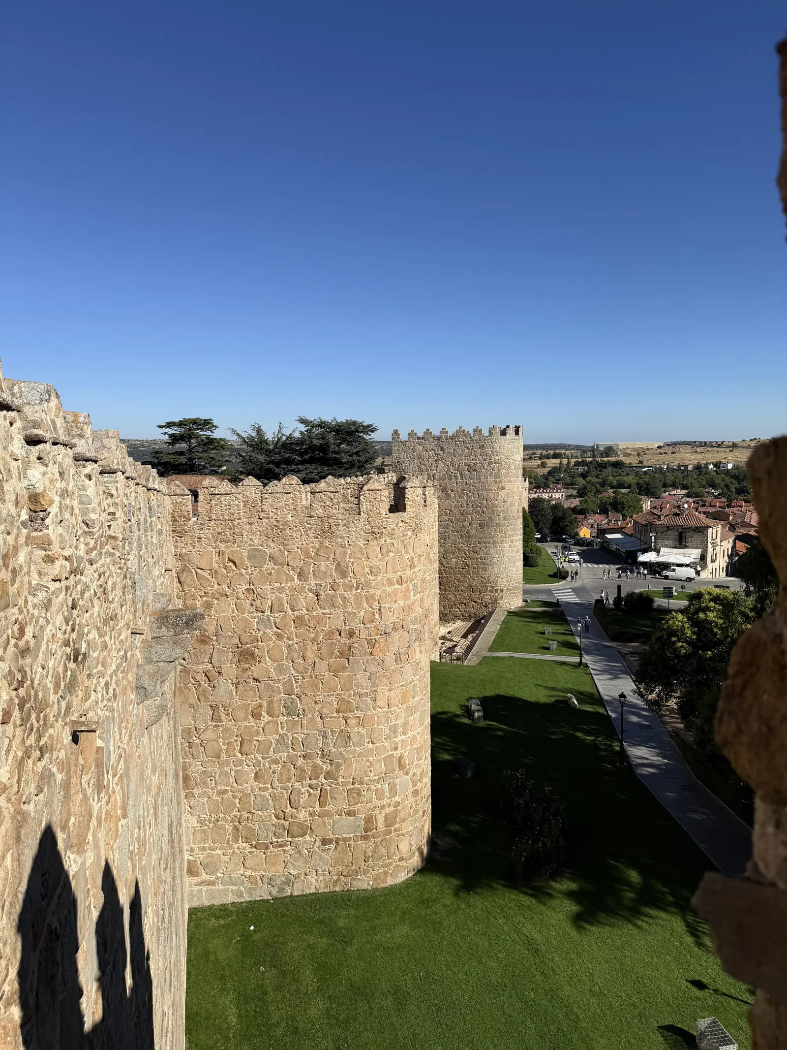 Cubos del lienzo norte de la muralla de Ávila vistos desde el adarve, con un jardín de césped y el paseo al pie. Foto propia La Maleta Inquieta, septiembre 2026.