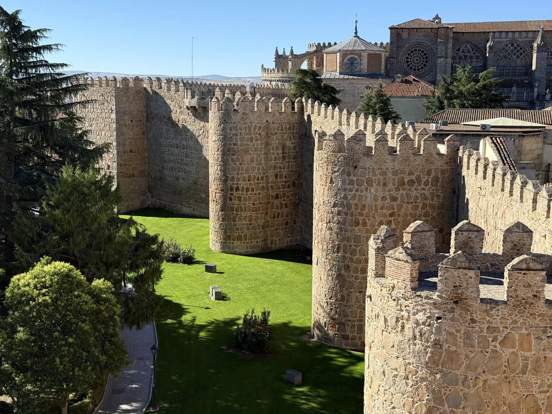 Cubos de la muralla de Ávila sobre un jardín de césped con la cabecera de la catedral al fondo, desde el adarve. Foto propia La Maleta Inquieta, septiembre 2026.