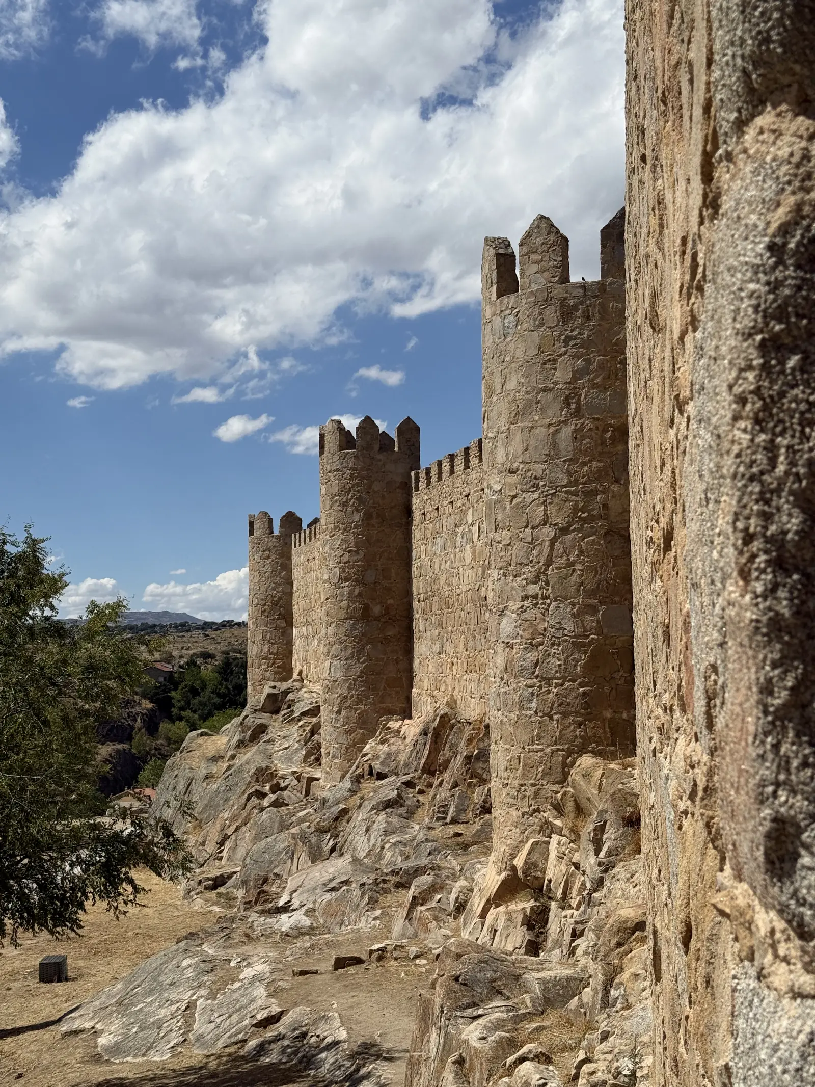 Cubos de la muralla sur de Ávila cimentados sobre la roca de granito, con el valle y nubes blancas al fondo. Foto propia La Maleta Inquieta, septiembre 2026.