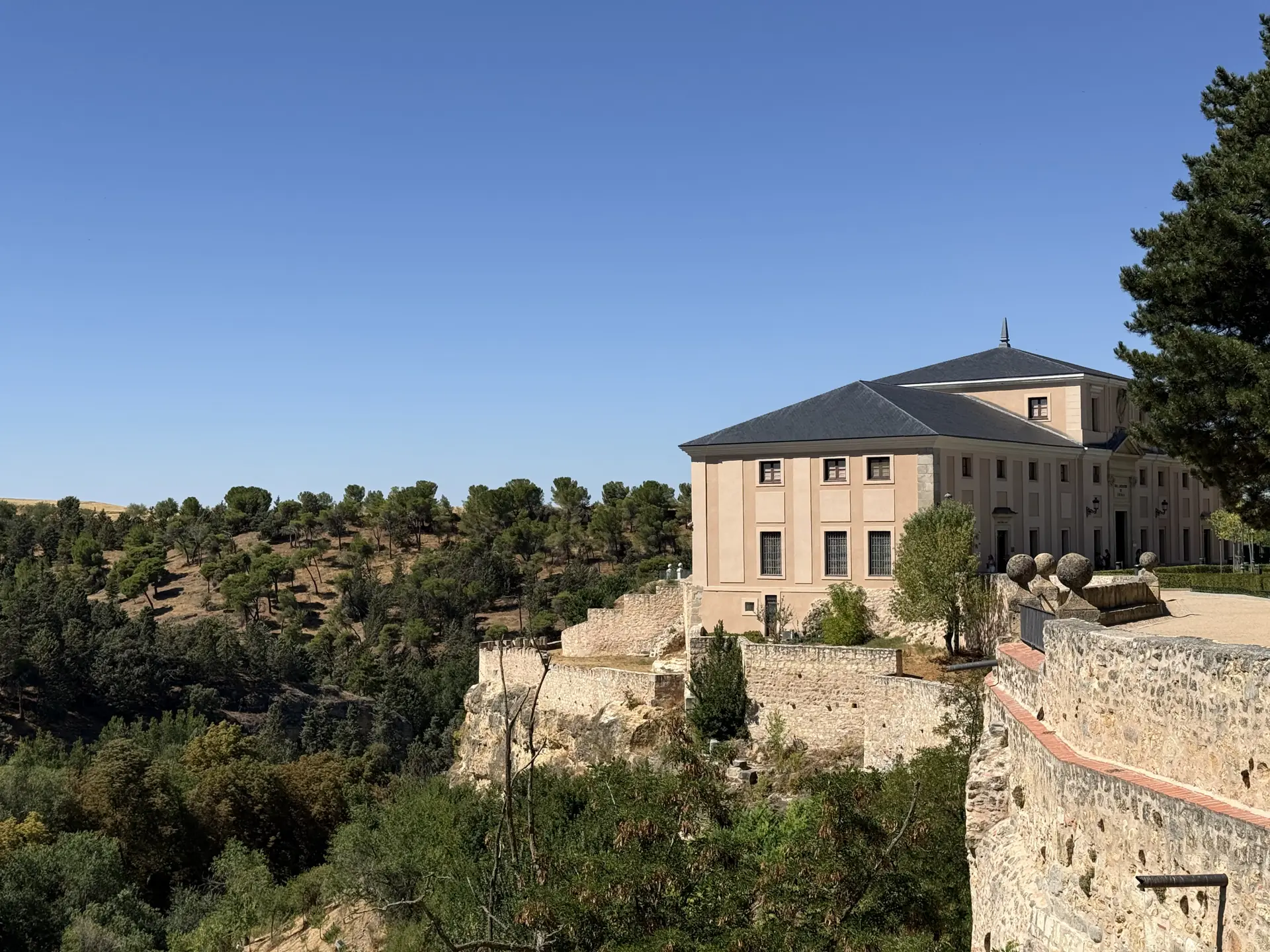 Edificio neoclásico asomado sobre la muralla de Segovia camino del Alcázar, entre encinas. Foto propia La Maleta Inquieta, septiembre 2026.