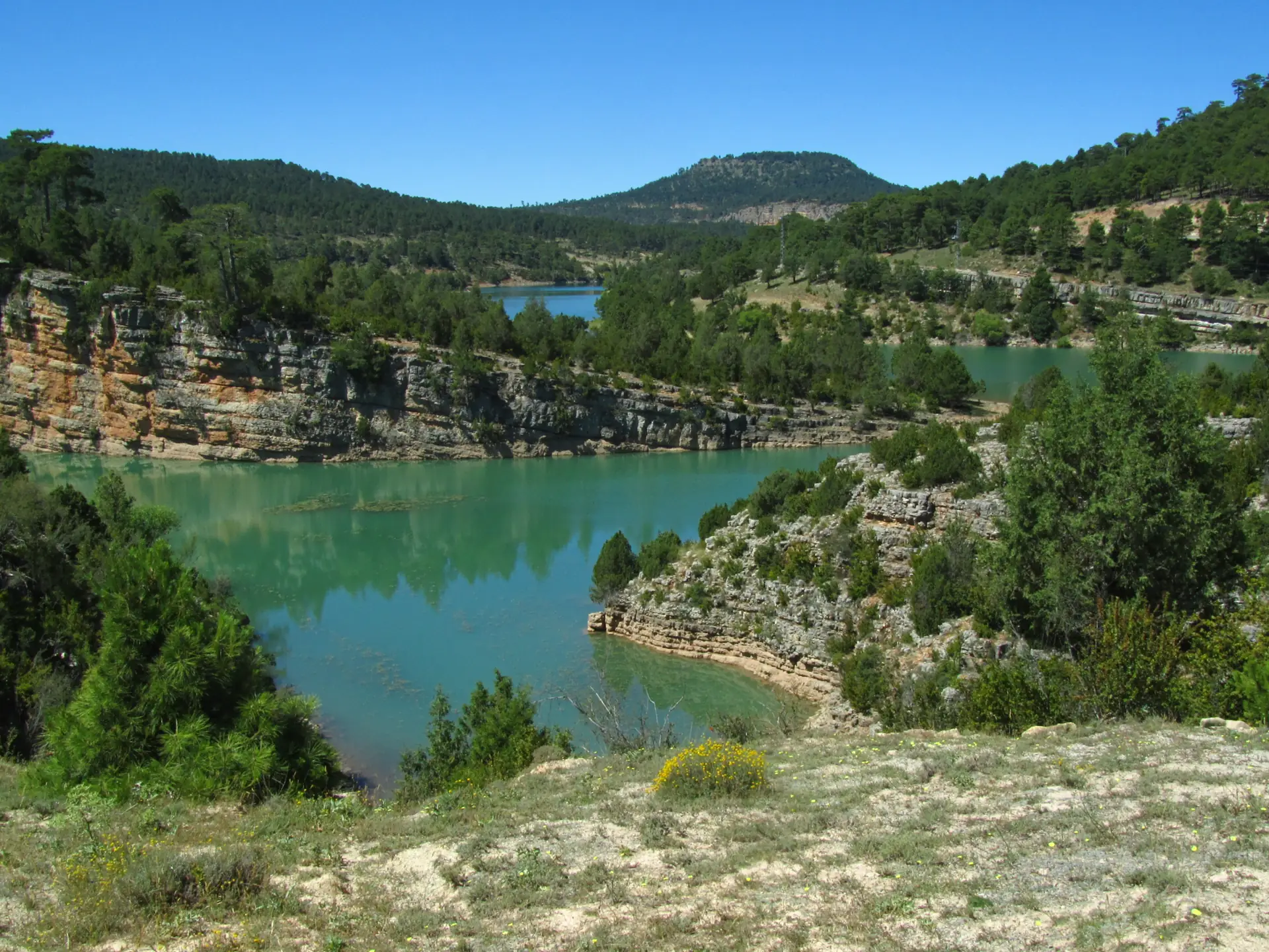 Embalse de La Toba, en la carretera del Nacimiento, con el agua turquesa entre orillas de roca y pinares.