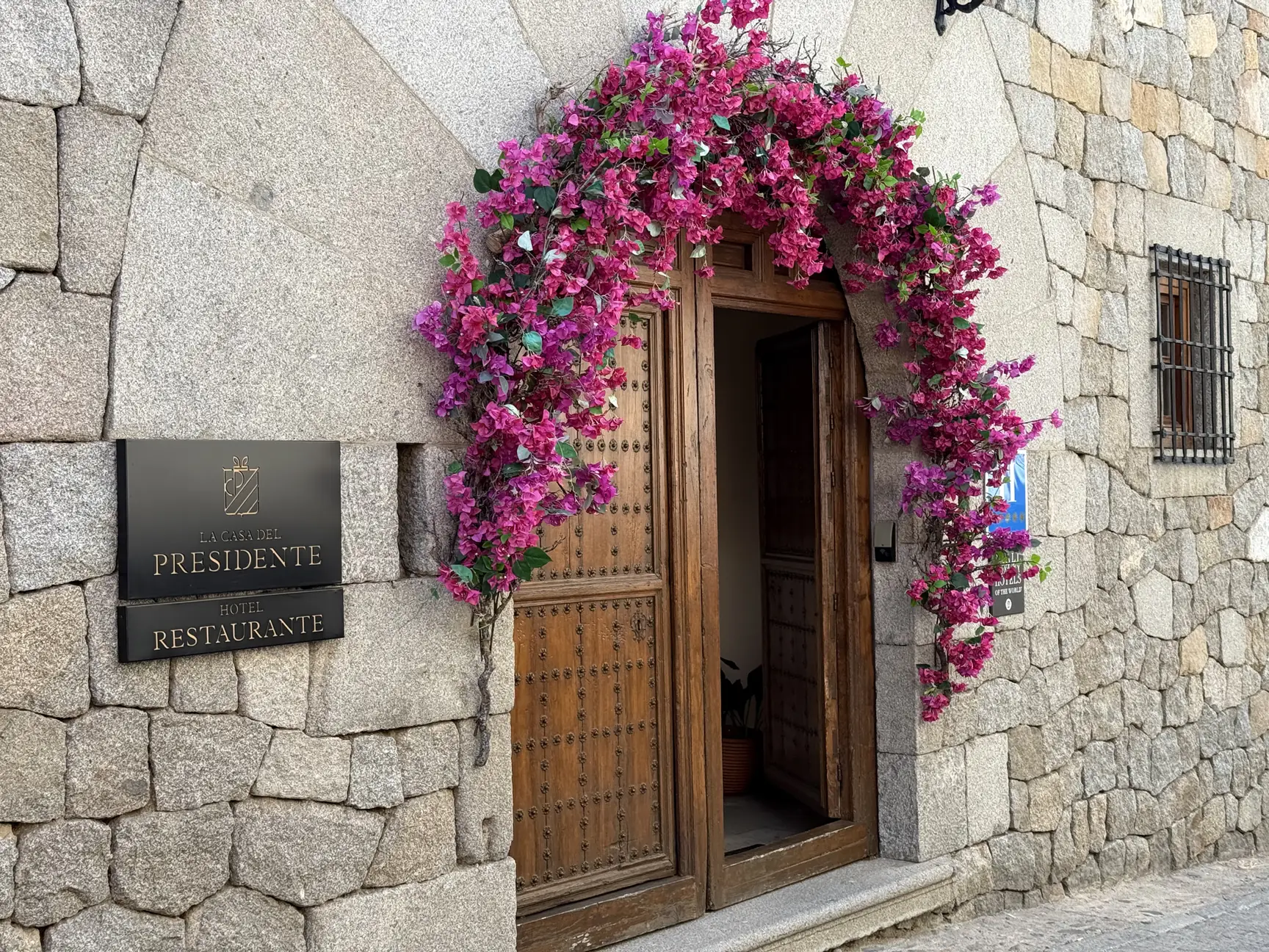 Puerta de madera claveteada con un arco de flores fucsias en la entrada del hotel La Casa del Presidente, Ávila. Foto propia La Maleta Inquieta, septiembre 2026.