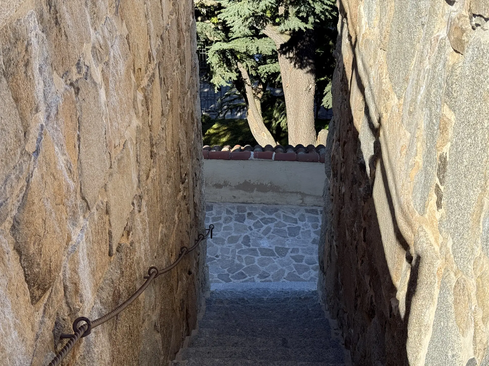 Escalera estrecha entre muros de granito con pasamanos de cadena de hierro en el recorrido del adarve de Ávila. Foto propia La Maleta Inquieta, septiembre 2026.