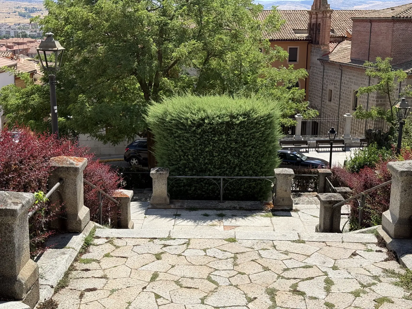 Escalinata ajardinada con setos hacia el barrio sur de Ávila, con una iglesia de espadaña de ladrillo al fondo. Foto propia La Maleta Inquieta, septiembre 2026.