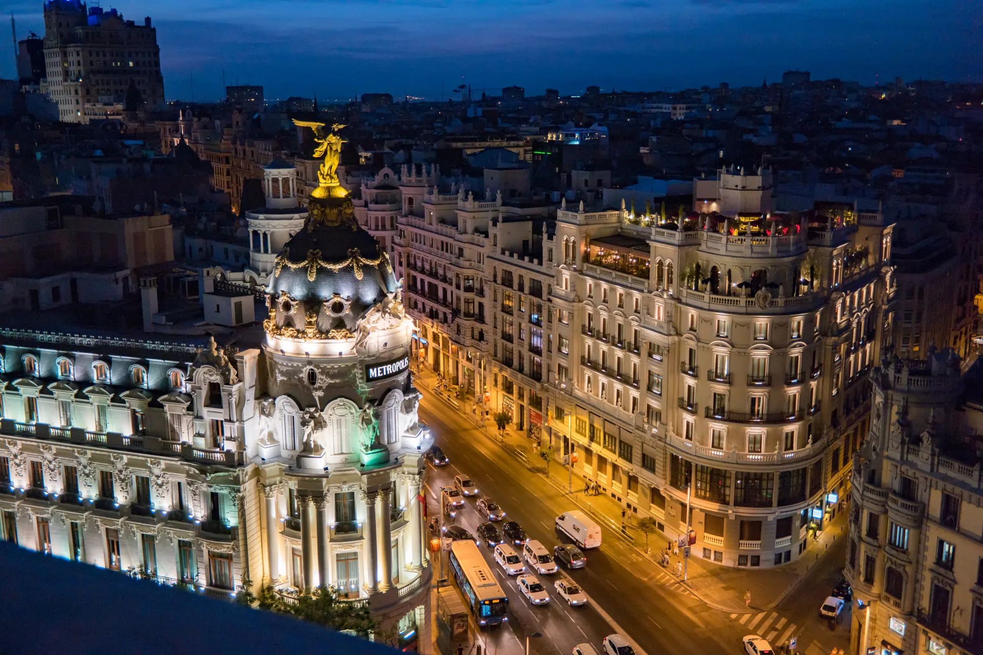 La Gran Vía de Madrid de noche vista desde una azotea, con la cúpula del Edificio Metrópolis iluminada y el tráfico de la avenida