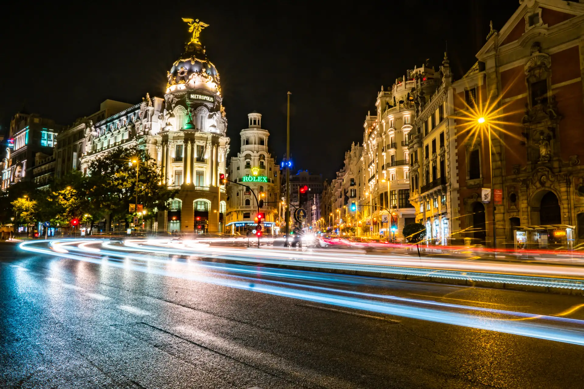 El Edificio Metrópolis iluminado de noche en el arranque de la Gran Vía de Madrid, con estelas de luz de los coches