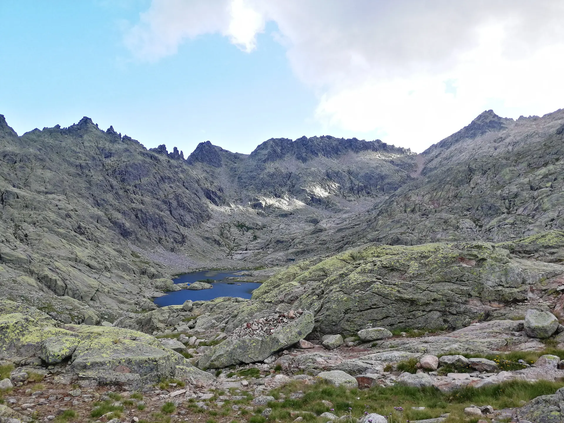 La Laguna Grande de Gredos al fondo del circo glaciar, rodeada de granito y pastos con mínima nieve residual, bajo los picos del Almanzor