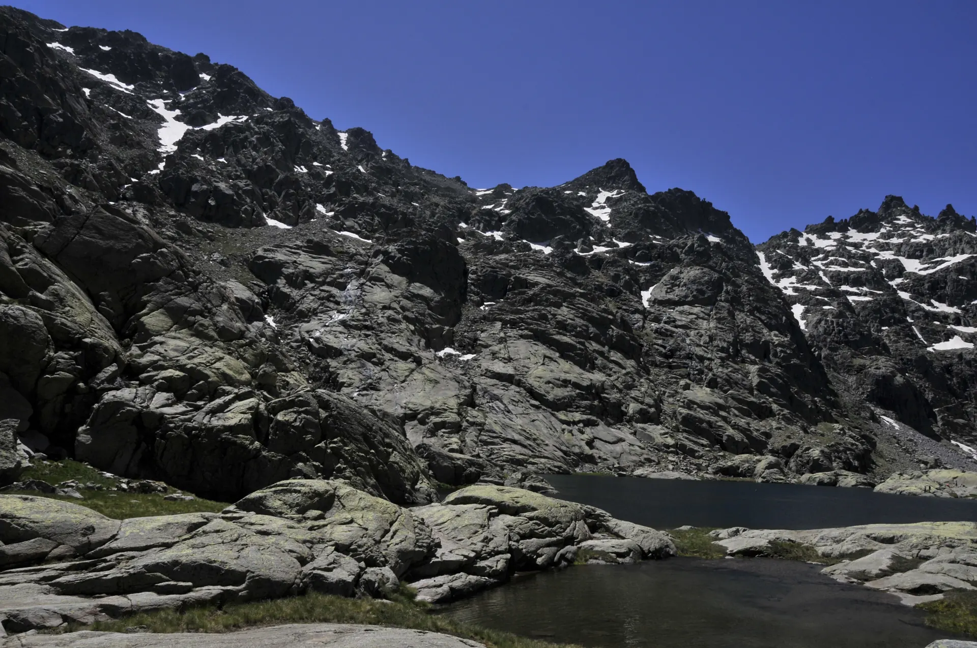 Desagüe de la Laguna Grande de Gredos entre bloques de granito, con las paredes del circo aún con neveros bajo el cielo azul