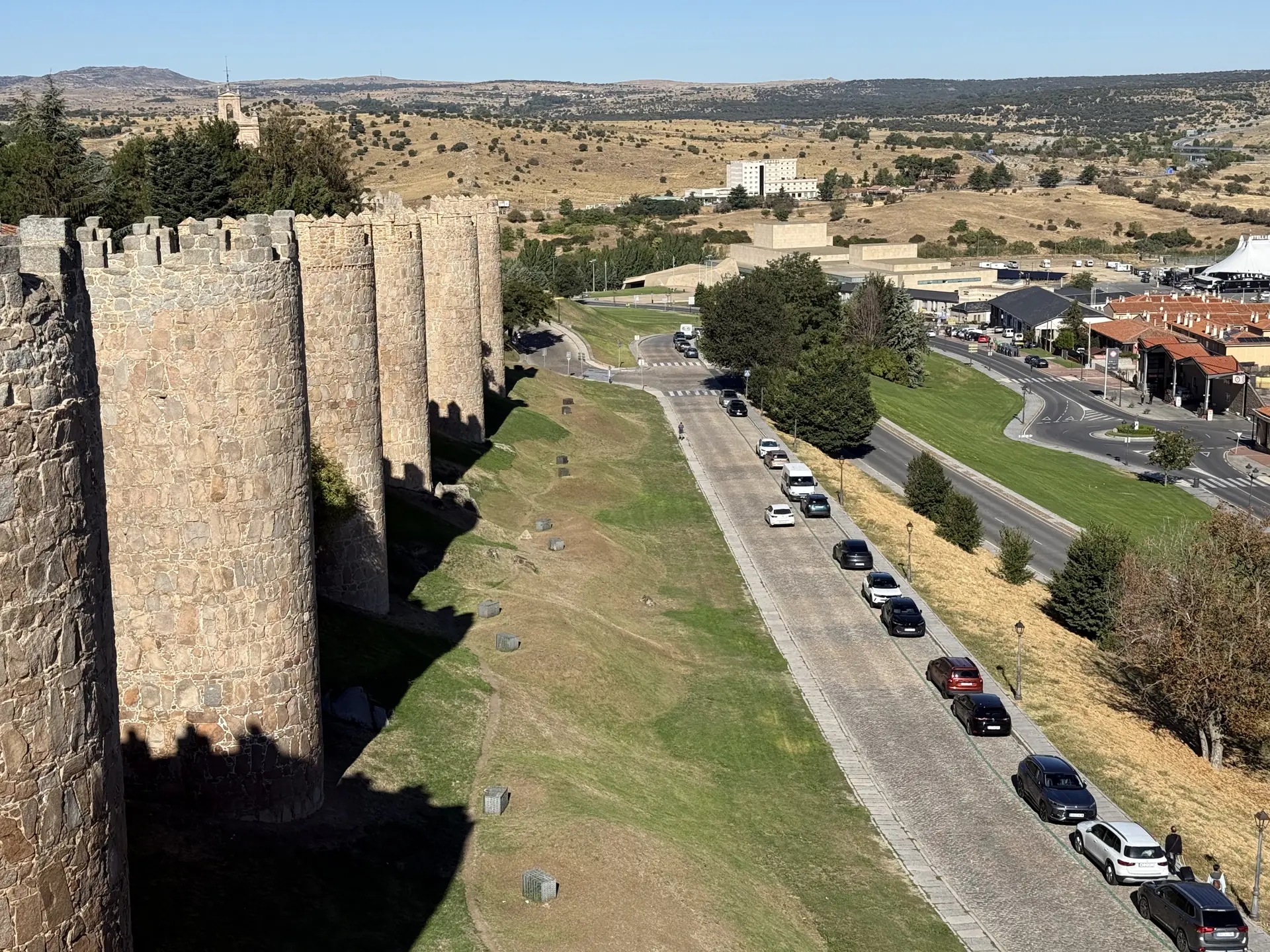 Cubos del lienzo norte de la muralla de Ávila con coches aparcados en la calle a su pie, vistos desde el adarve. Foto propia La Maleta Inquieta, septiembre 2026.