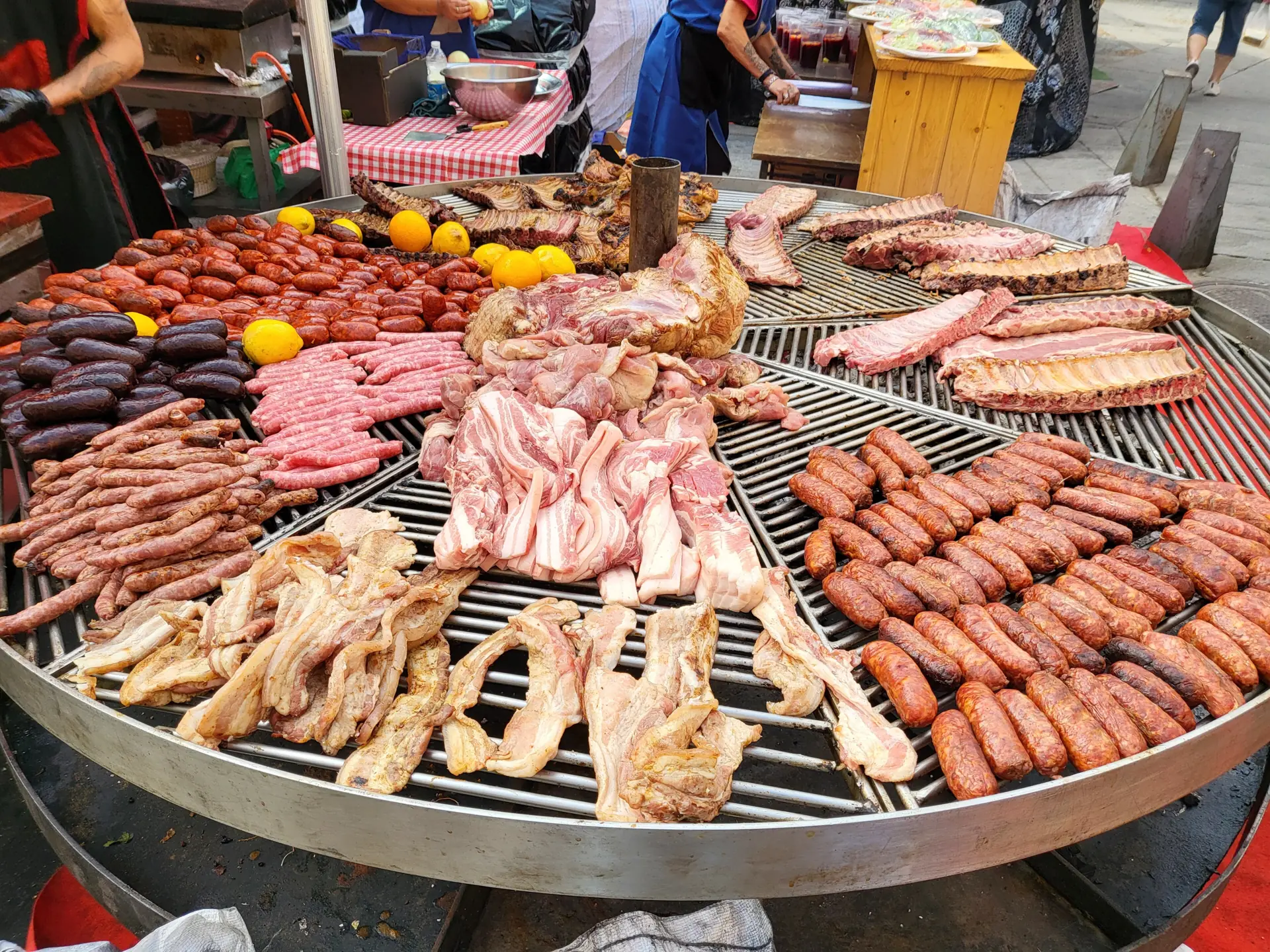 Gran parrilla redonda con chorizos, morcillas, panceta y costillas asándose en un puesto del Mercado Medieval de Ávila