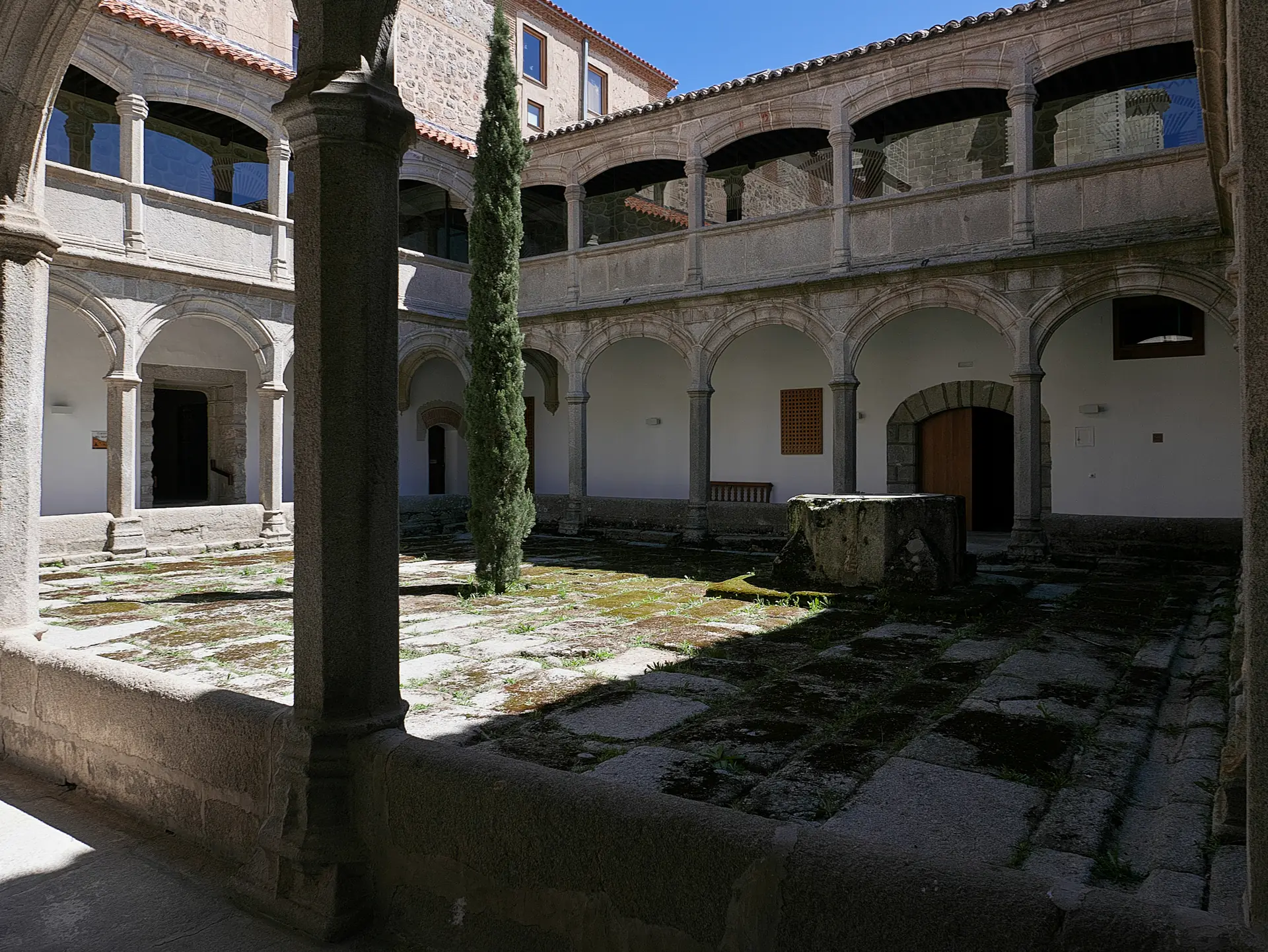 Claustro del Noviciado del monasterio de Santo Tomás de Ávila, sobrio, con dos pisos de arcos de granito, pozo de piedra y un ciprés en el patio