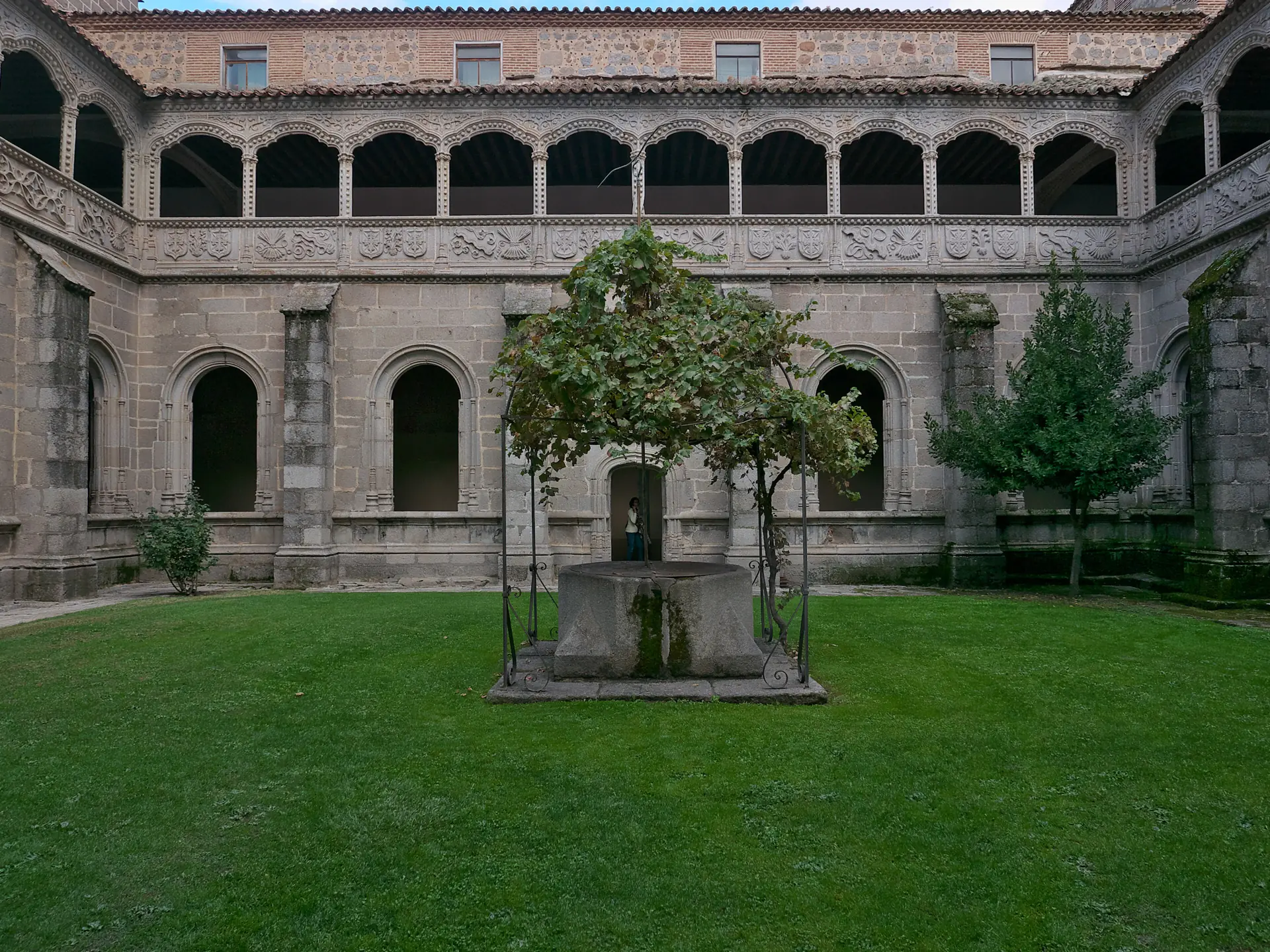 Claustro del Silencio del Real Monasterio de Santo Tomás de Ávila, con dos pisos de arcos de granito y jardín con árbol en el centro