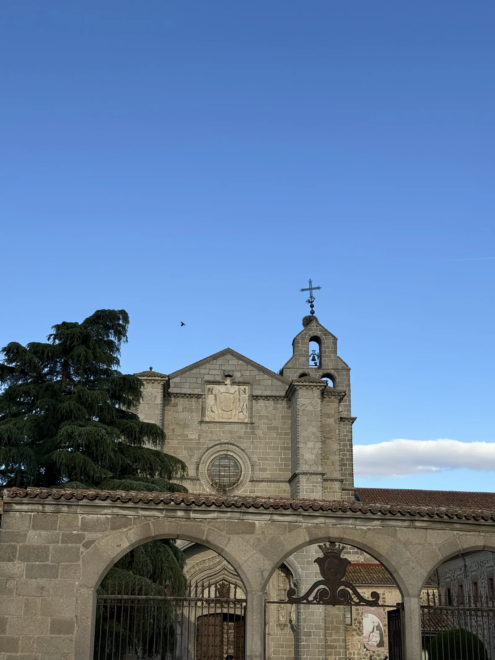 Hastial y espadaña con nido de cigüeña del monasterio de Santo Tomás de Ávila, tras los arcos y la verja del atrio. Foto propia La Maleta Inquieta, septiembre 2026.