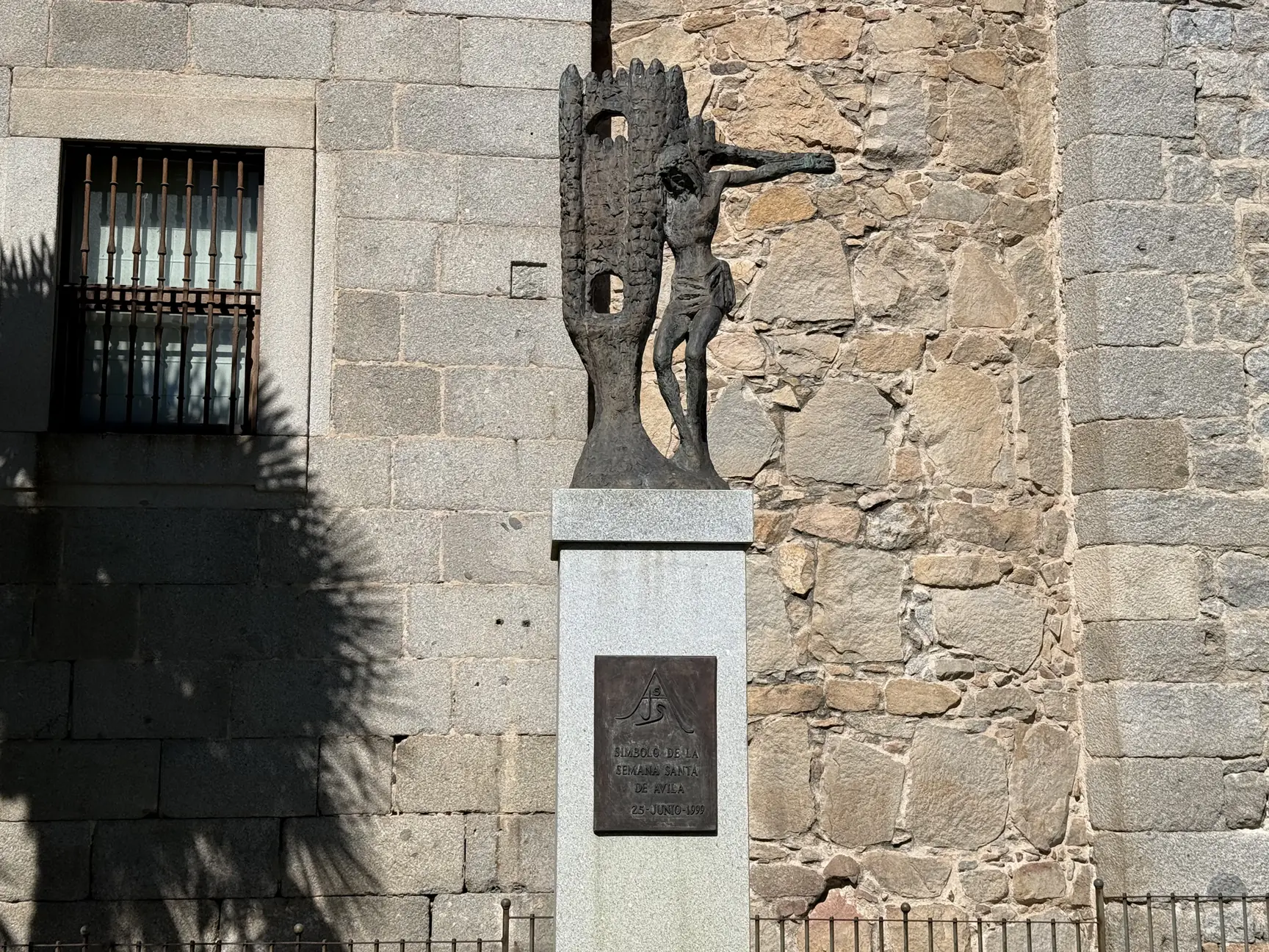 Monumento Símbolo de la Semana Santa de Ávila, un Cristo de bronce junto a una torre, ante un muro de granito. Foto propia La Maleta Inquieta, septiembre 2026.