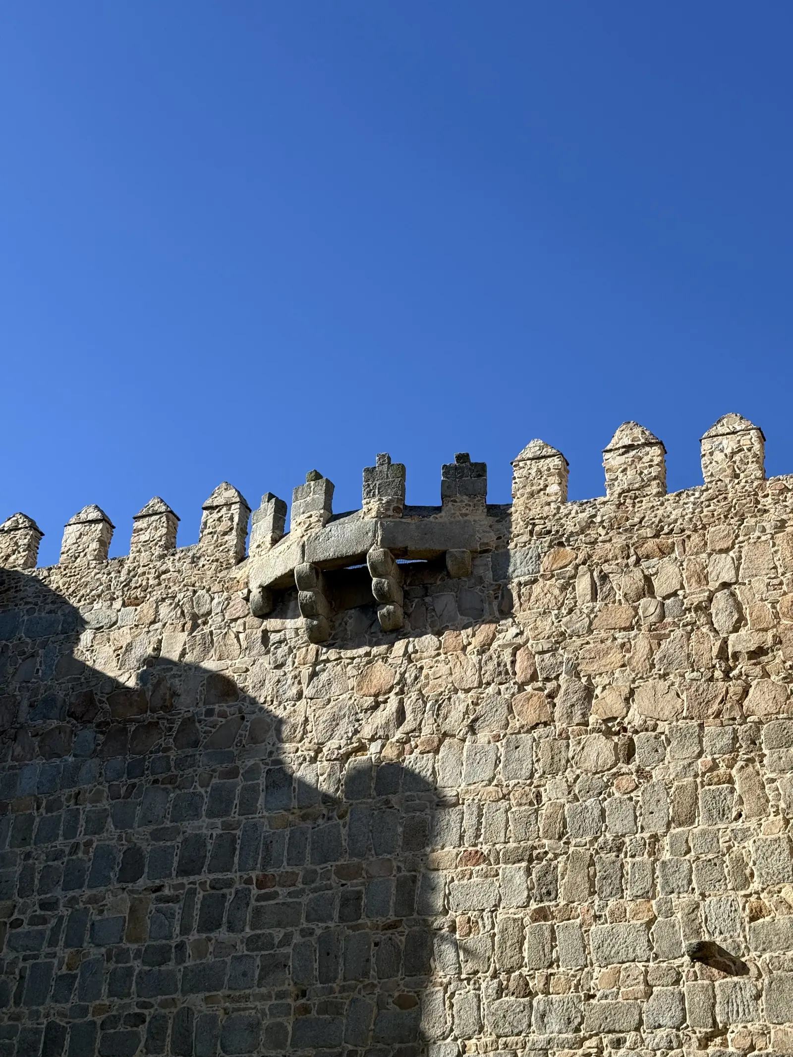 Almenas y matacán de granito del lienzo oriental de la muralla de Ávila, con su sombra y cielo azul. Foto propia La Maleta Inquieta, septiembre 2026.