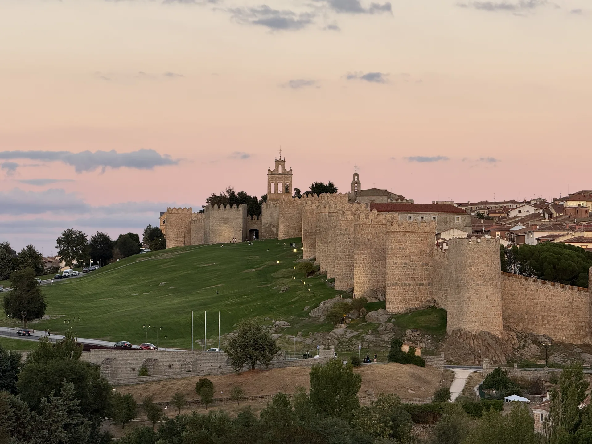 Muralla de Ávila y espadaña de la Puerta del Carmen bajo un cielo rosa tras la puesta de sol, desde Cuatro Postes. Foto propia La Maleta Inquieta, septiembre 2026.