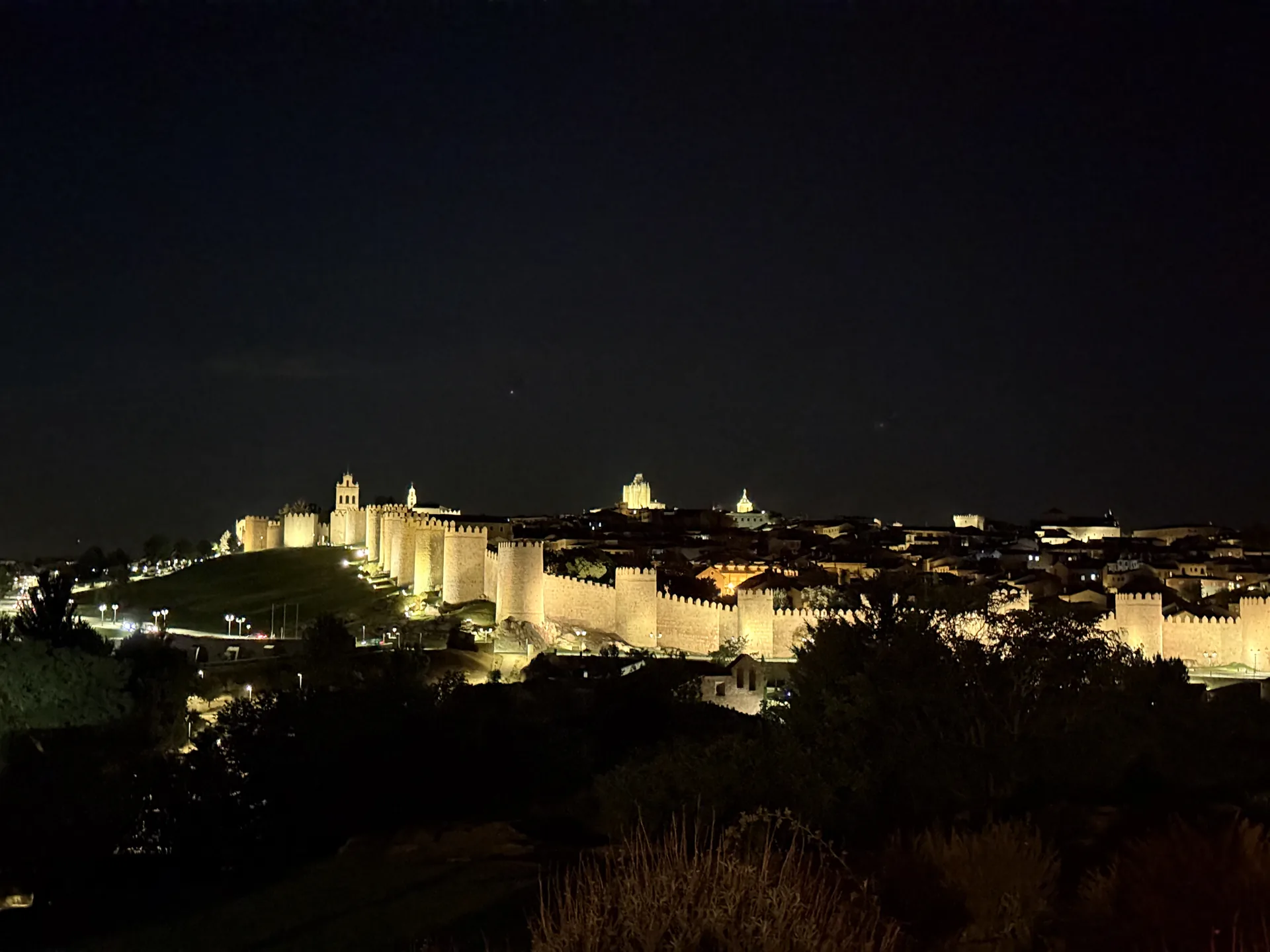 Muralla de Ávila iluminada de noche con la torre de la catedral y la espadaña del Carmen, desde Los Cuatro Postes. Foto propia La Maleta Inquieta, septiembre 2026.