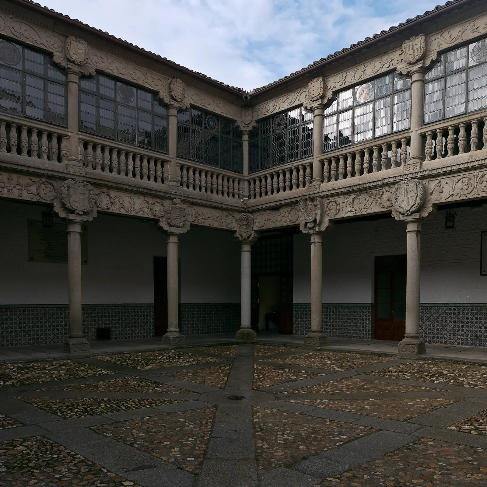 Patio renacentista del palacio de Polentinos de Ávila, con columnas de granito, escudos tallados, galería acristalada y suelo de canto rodado