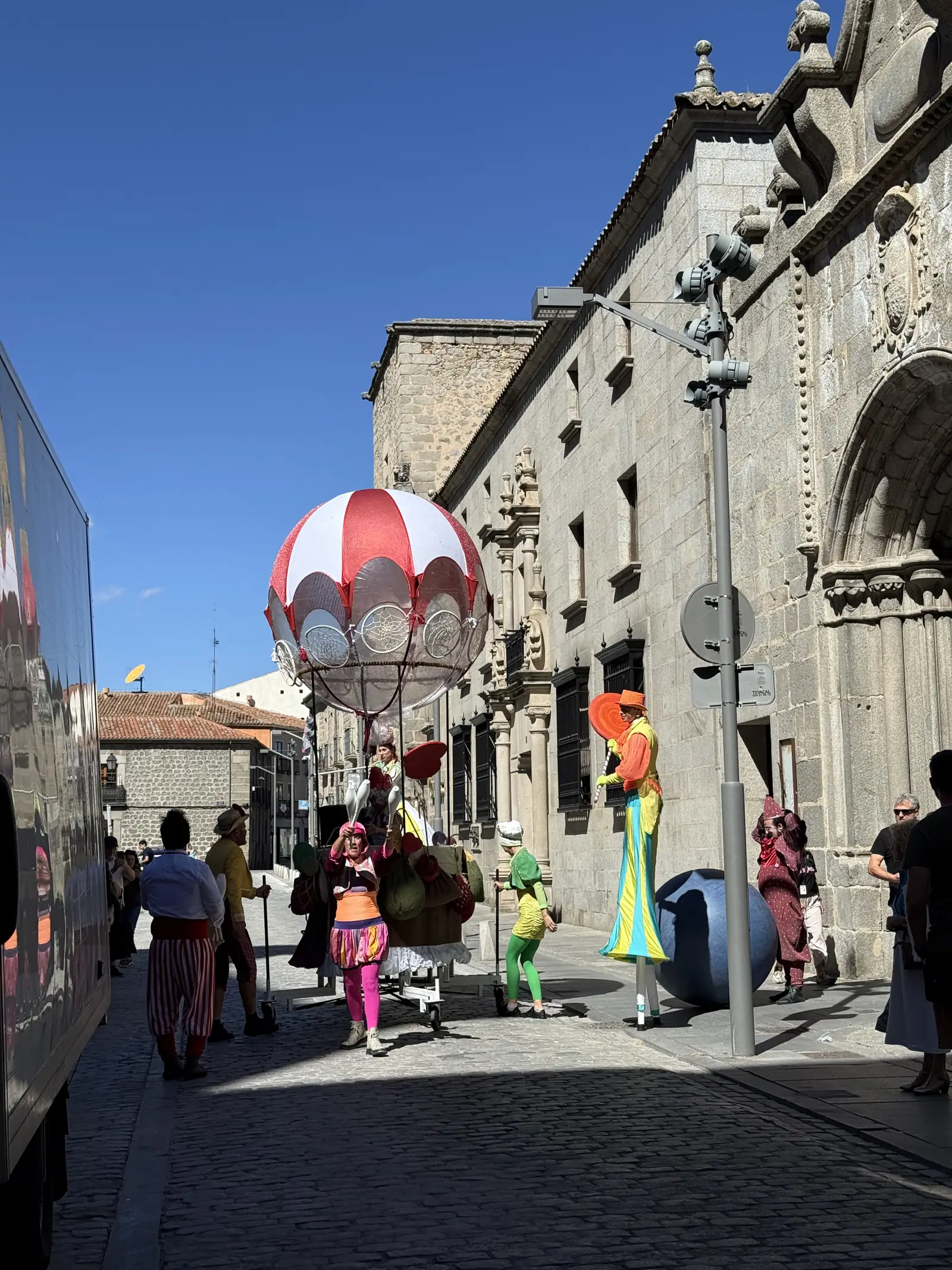 Pasacalles con zancudos de colores y una carroza en forma de globo en una calle empedrada de Ávila. Foto propia La Maleta Inquieta, septiembre 2026.