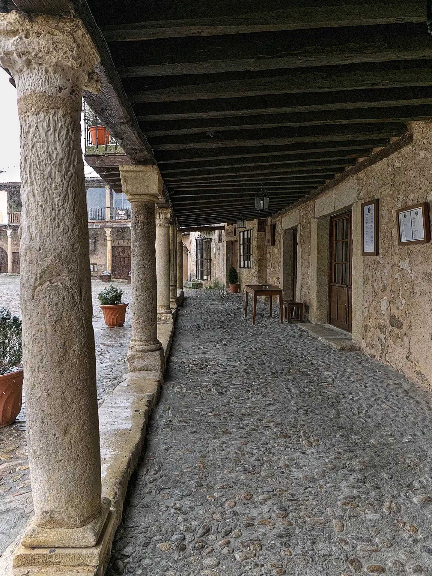 Soportales de la Plaza Mayor de Pedraza, con las columnas de piedra y las vigas de madera sobre el empedrado.