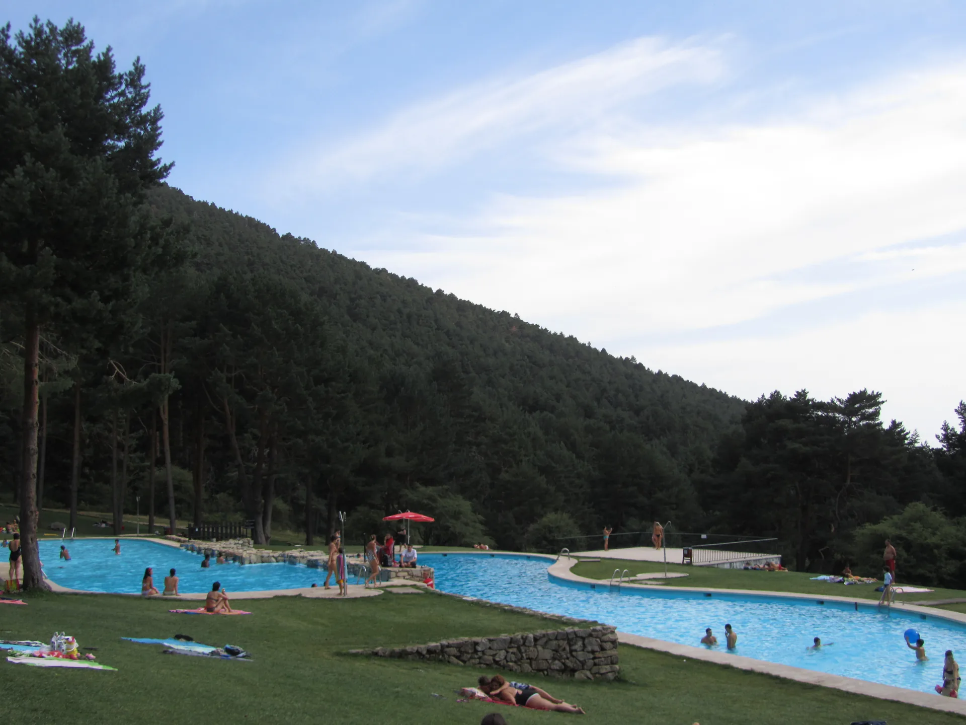 Piscinas naturales de Las Berceas en Cercedilla, con bañistas en el césped y el pinar de la sierra detrás