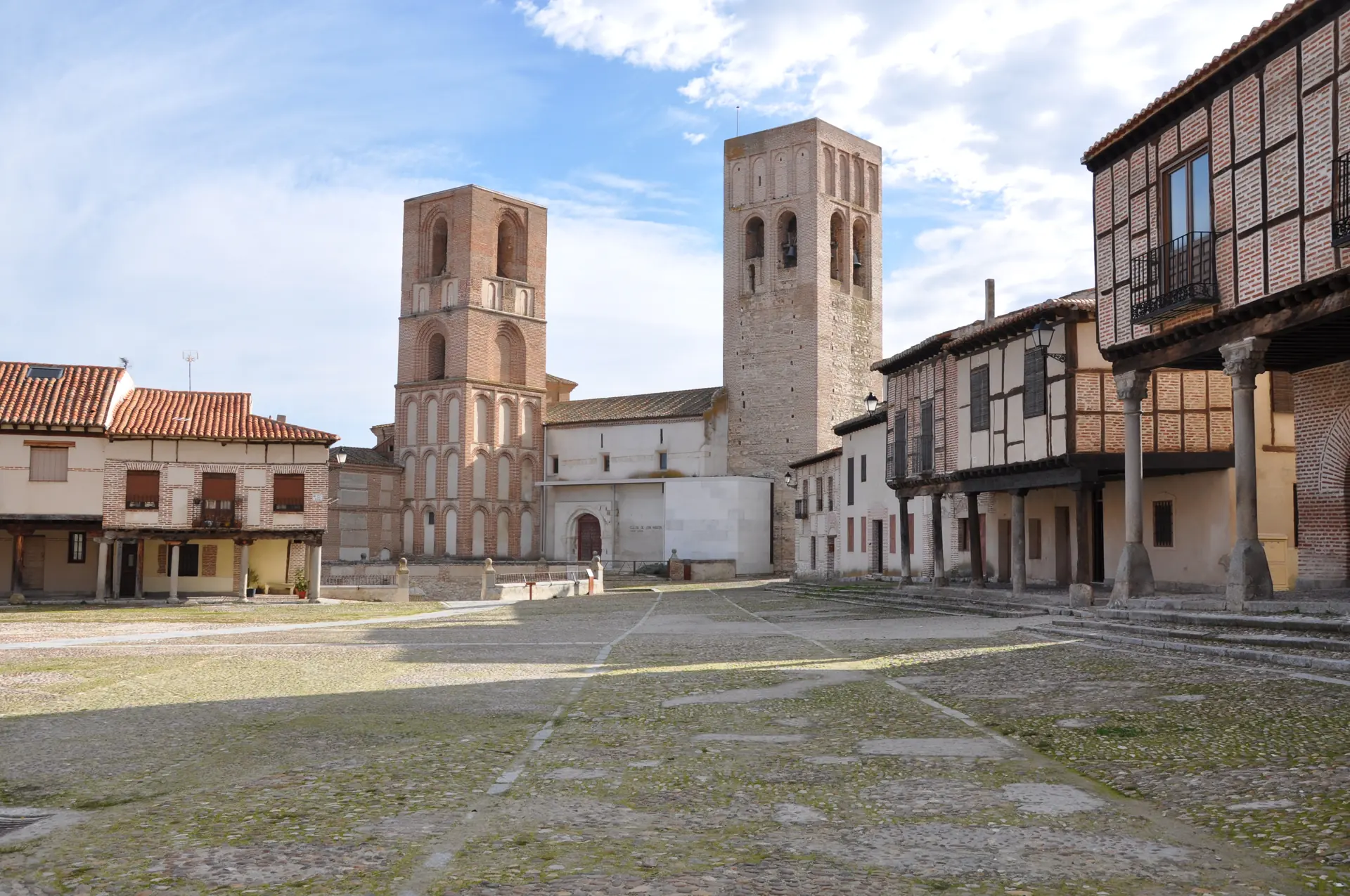 Plaza de la Villa de Arévalo empedrada, con casas porticadas de ladrillo y entramado y las dos torres mudéjares de la iglesia de San Martín al fondo